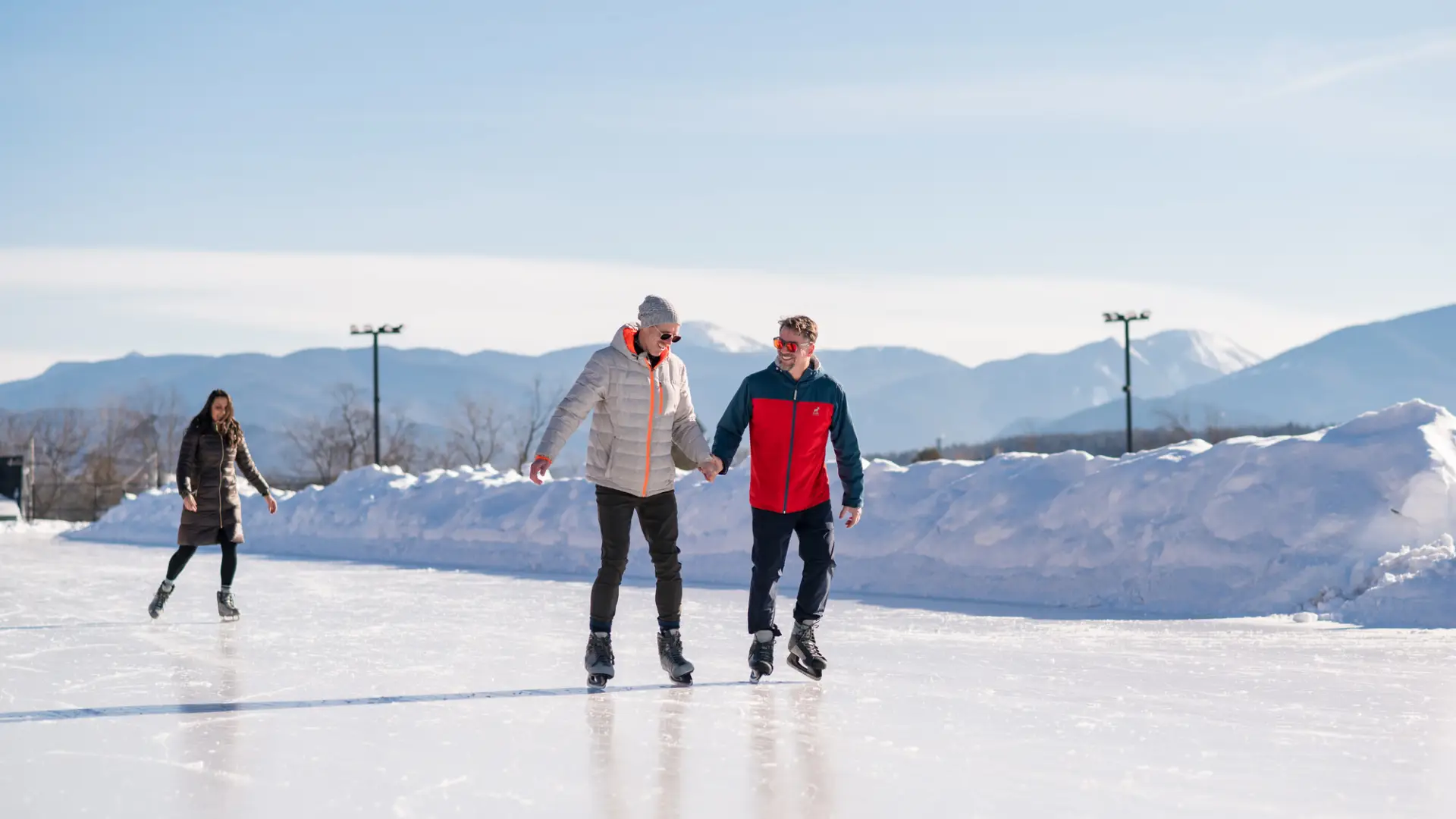 Two men ice skate on outdoor track holding hands