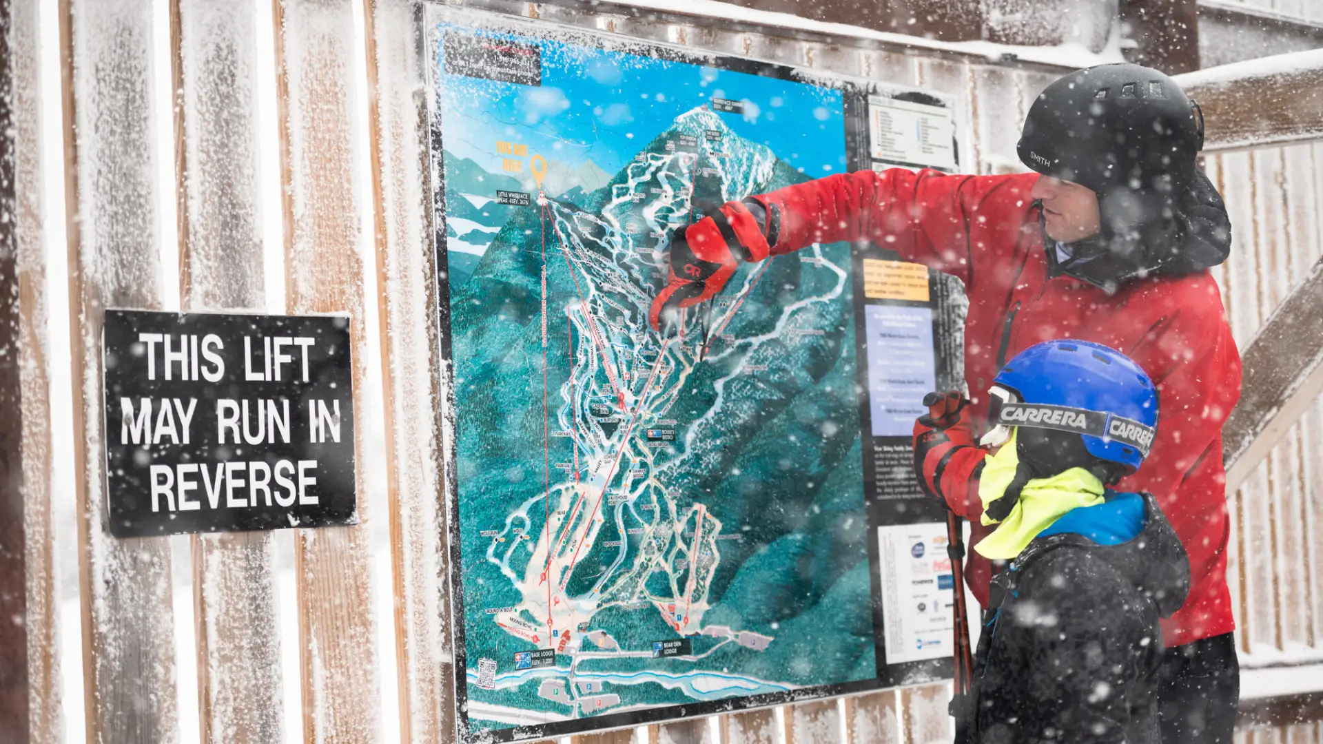A father pointing out something on a ski mountain map to his kid