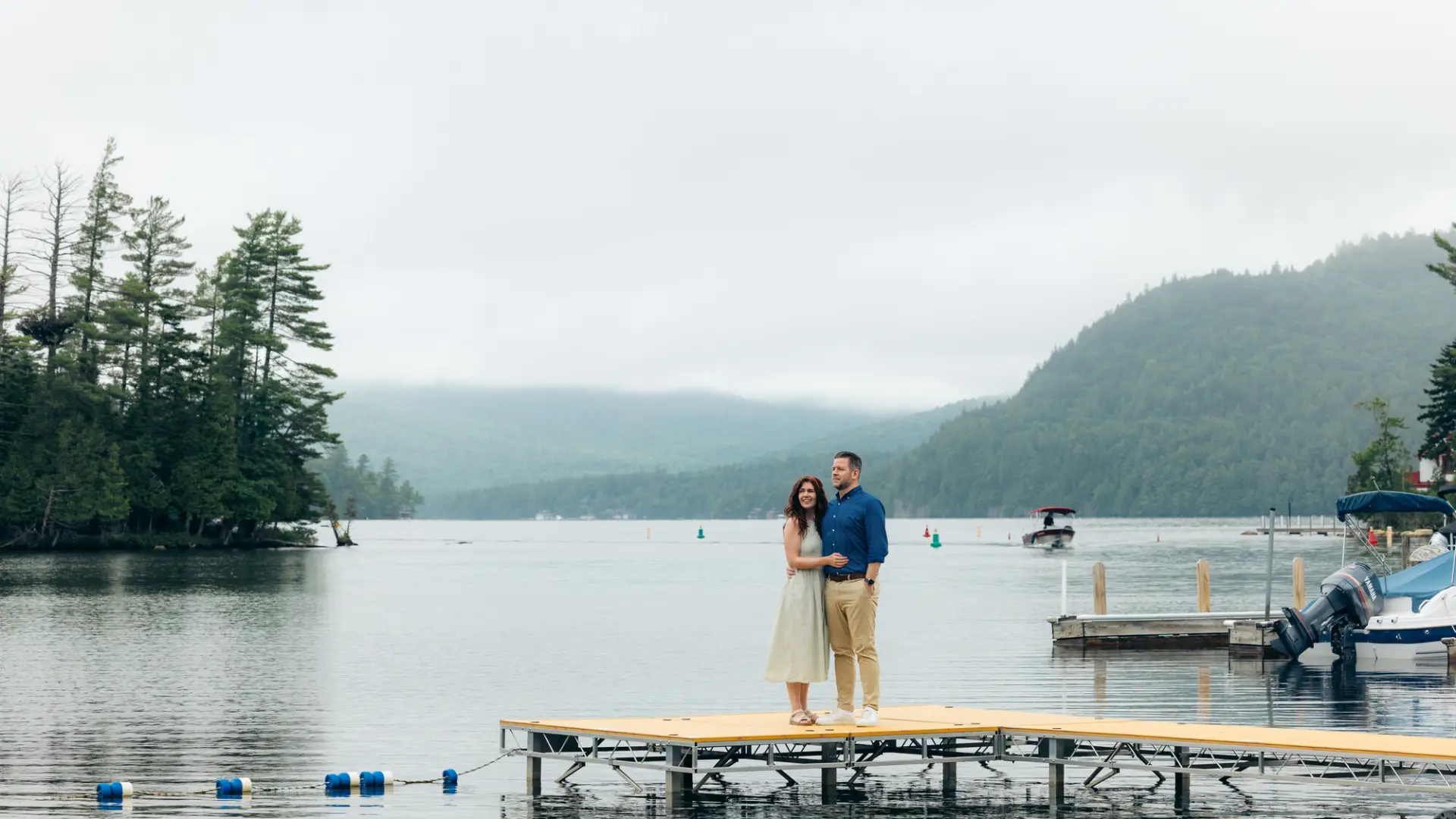 Couple stands on dock of a misty Adirondack lake in summer
