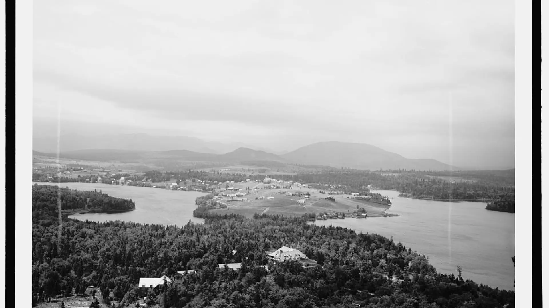 A vintage black and white aerial photo of forest, lakes, and a small village from the early 20th century.