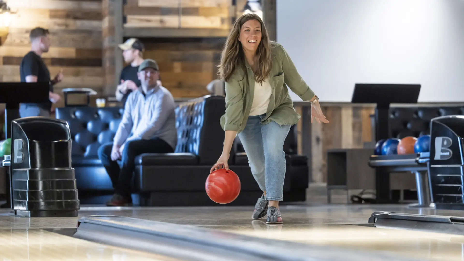A woman prepares to release a bowling ball on a wood alley at a hip bowling alley.