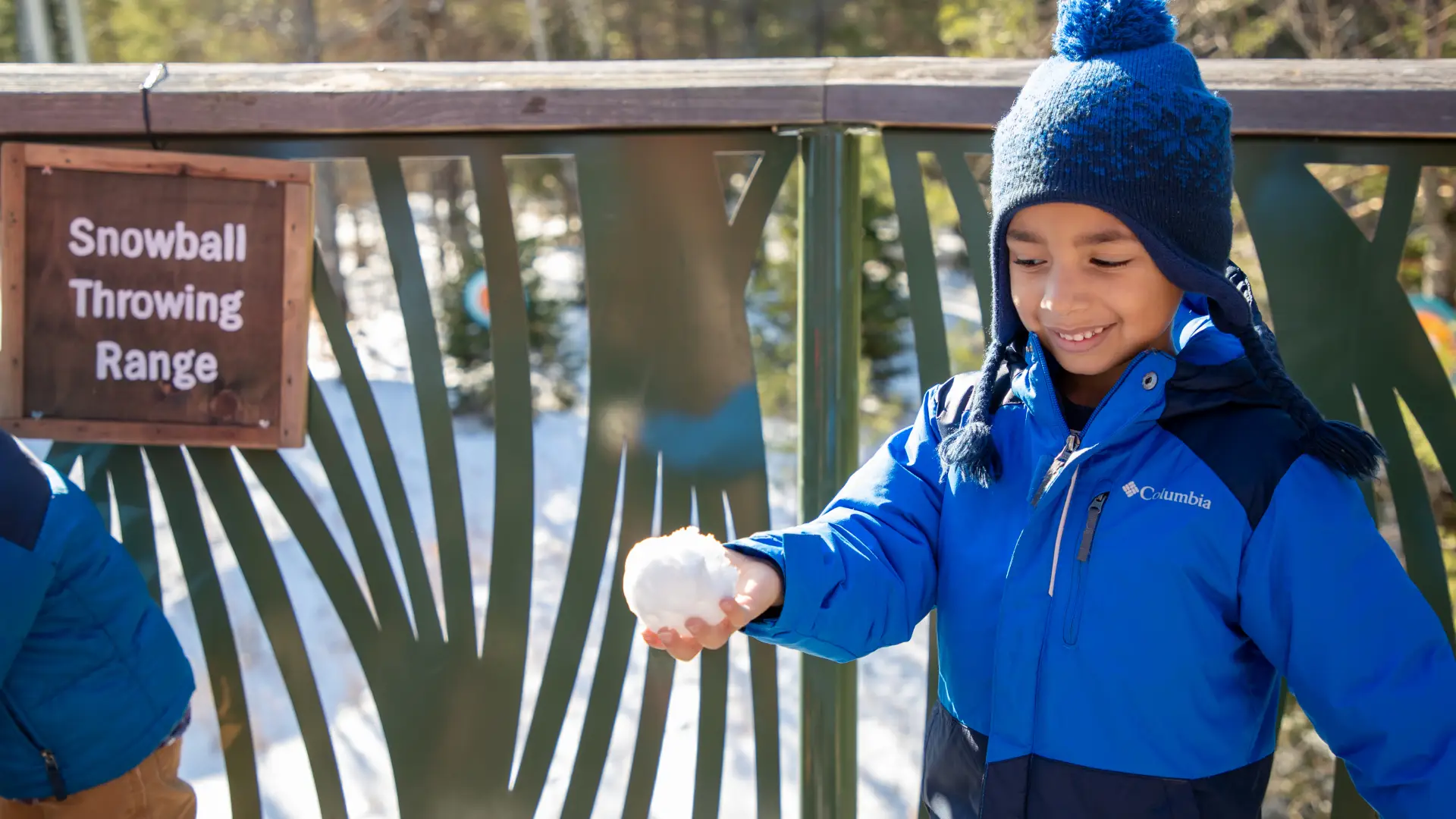 A young child gleefully looks down at his hand holding a freshly made snowball