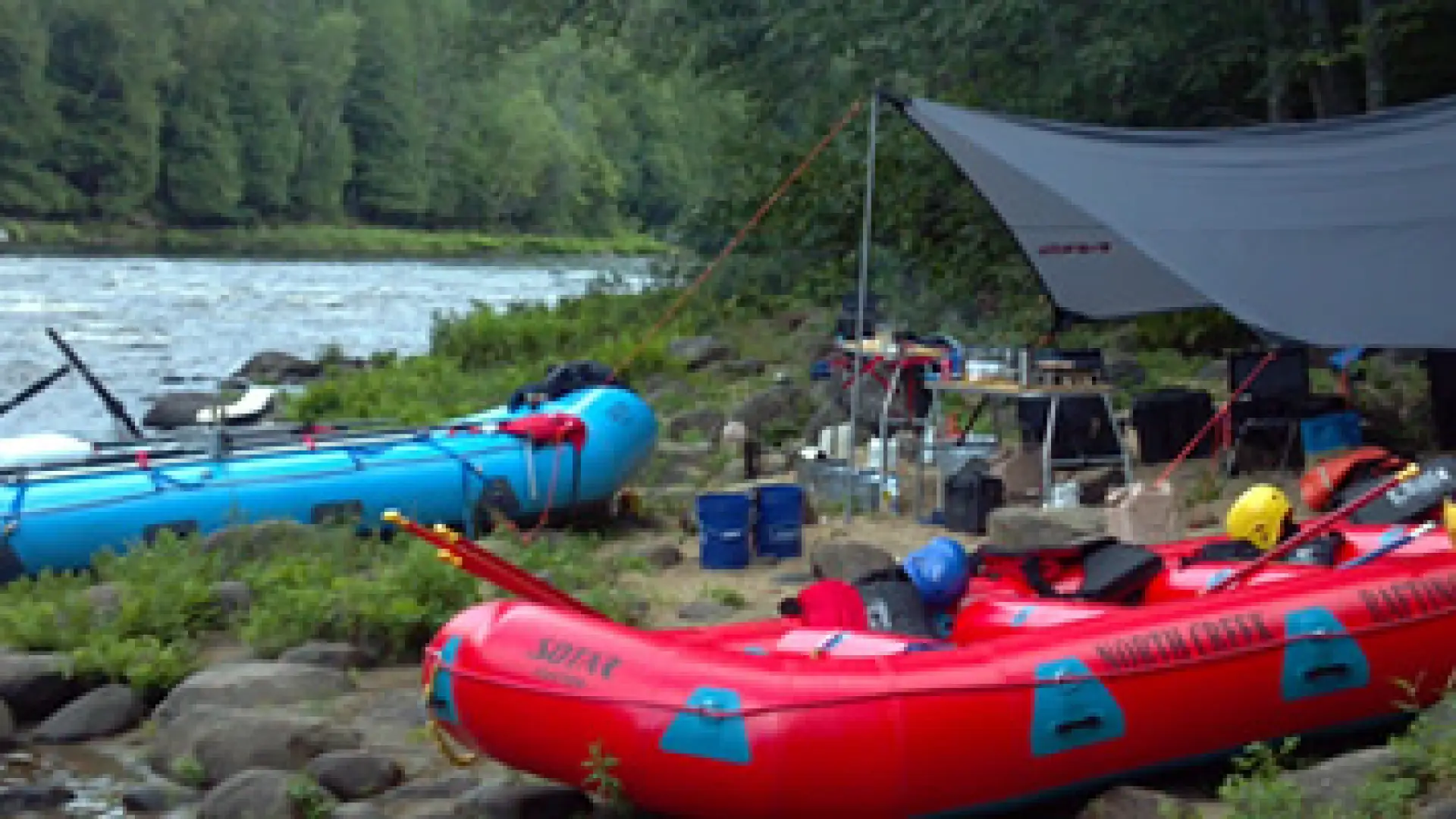 Inflatable rafts on the edge of the river with tents in the background