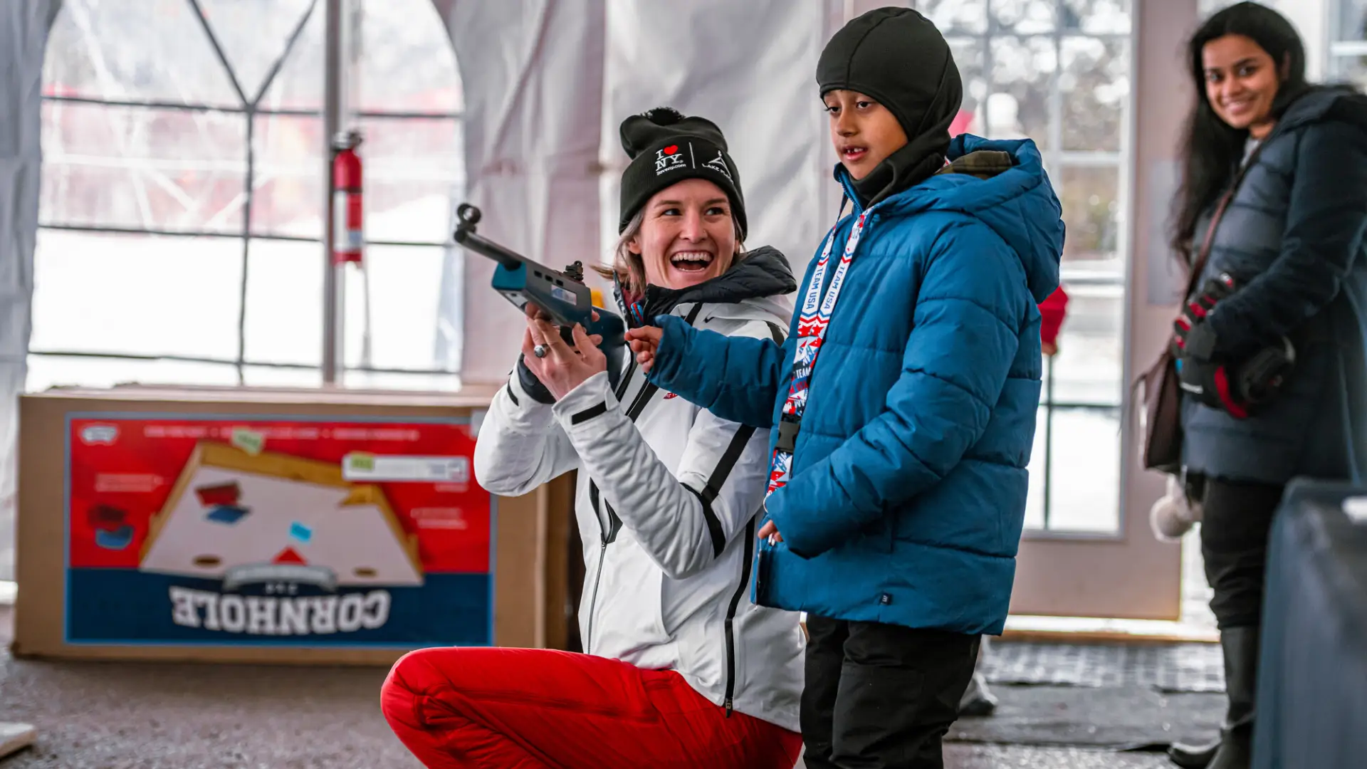 A female biathlete shows her rifle to a child at a biathlon event.