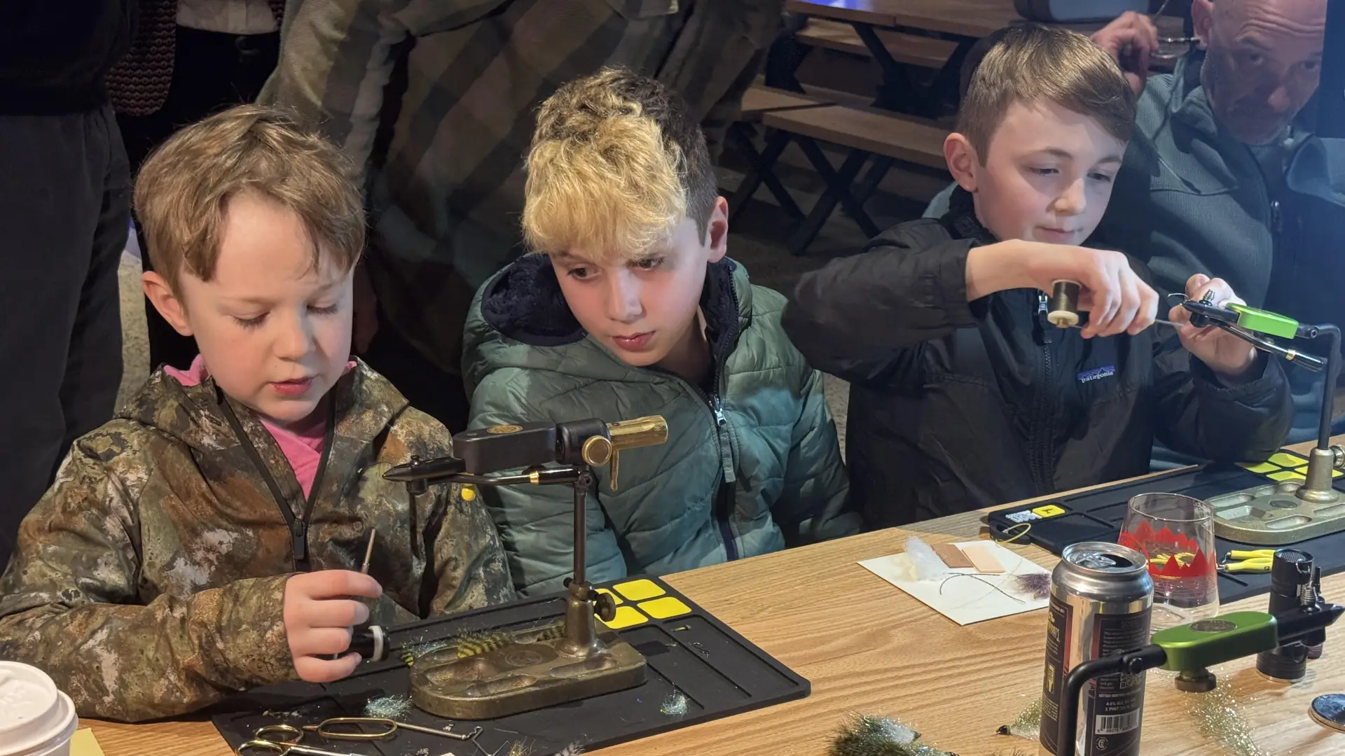 Three kids tying fly fishing flies at table