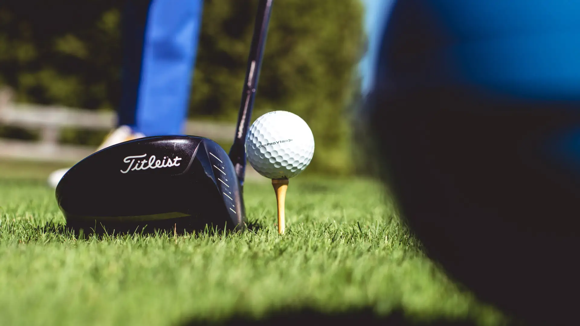 Golf ball on tee with driving club lined up on green grass
