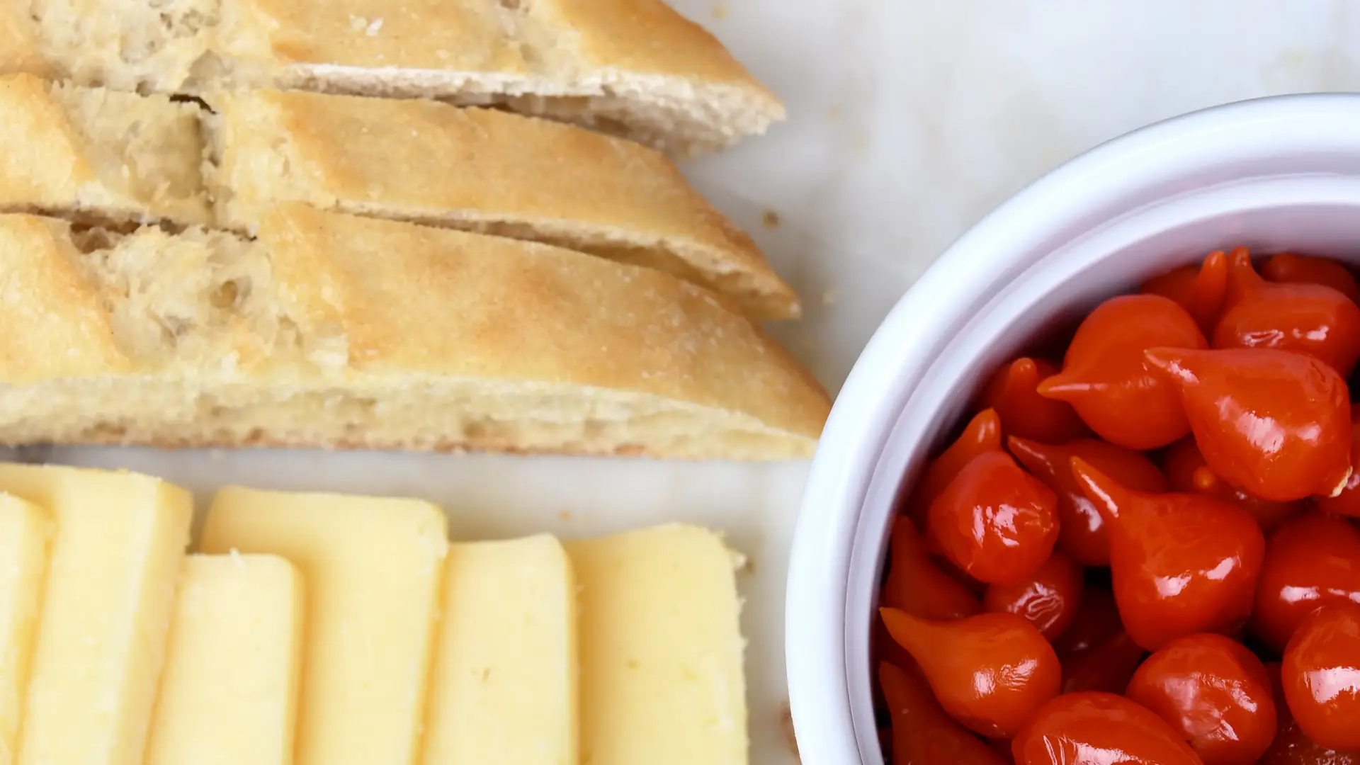 Charcuterie board with bread, cheese and bowl of red peppers