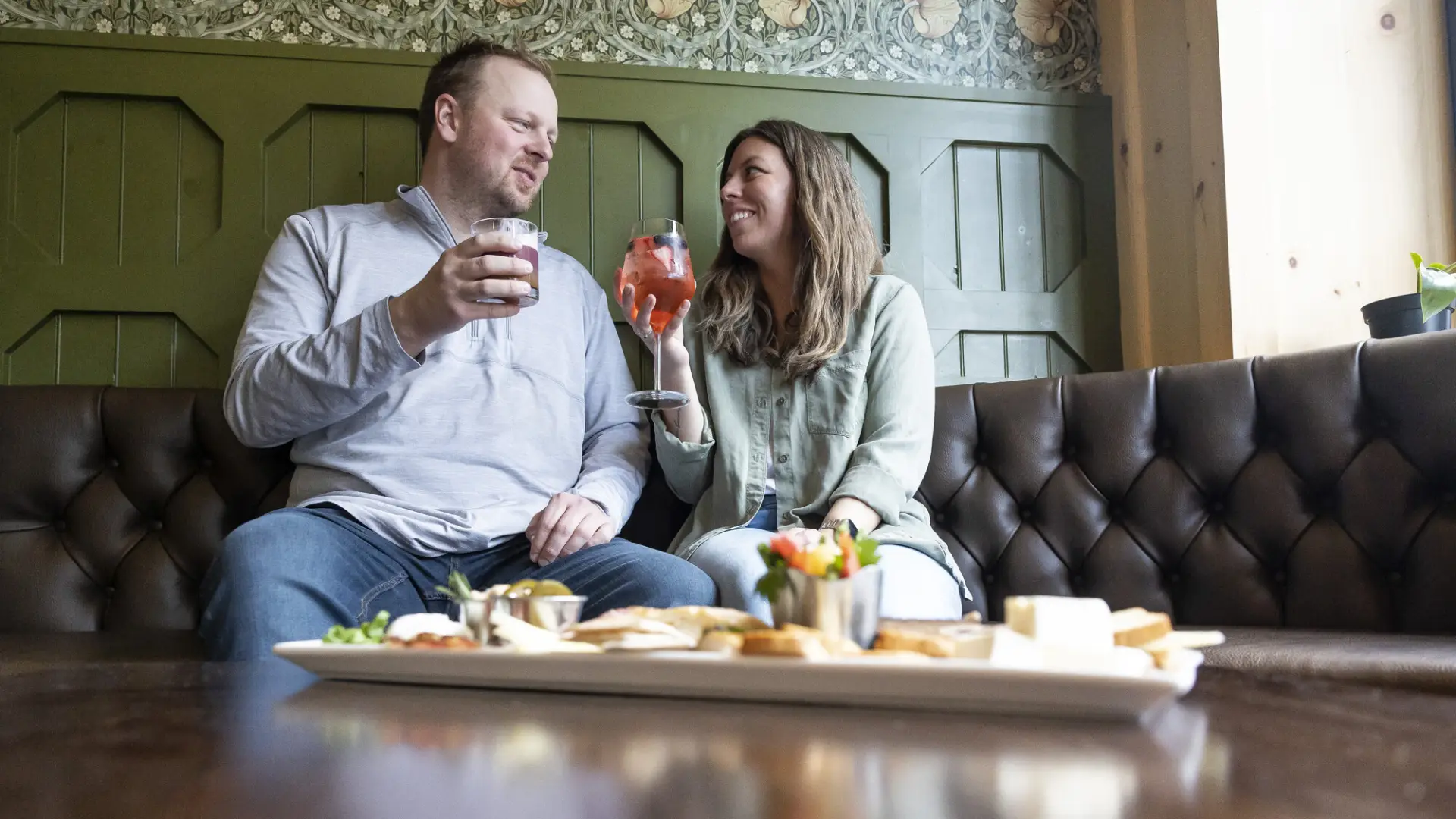 A man woman share drinks at a bar booth. 