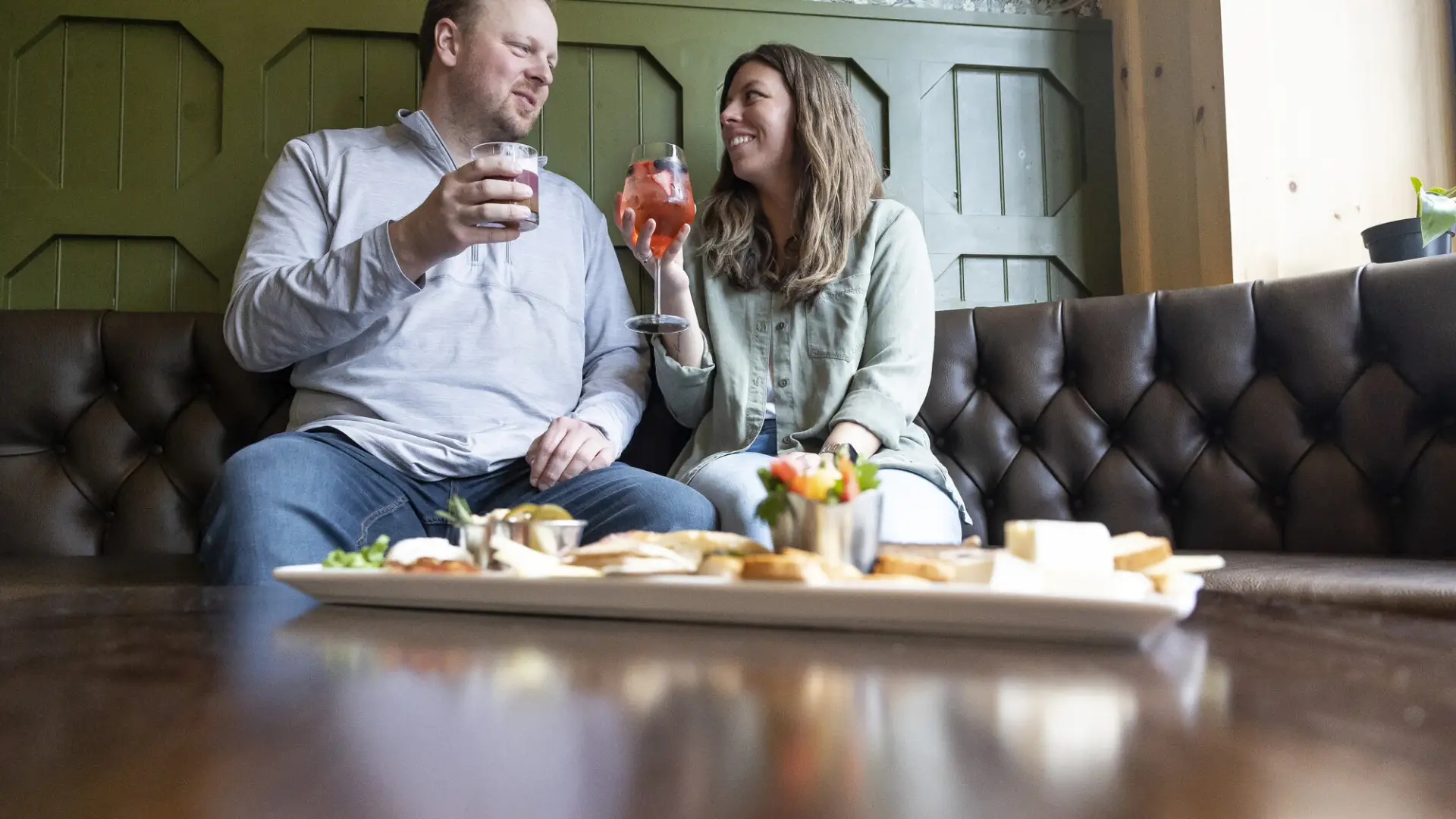 A man and woman share cocktails and a charcuterie board.