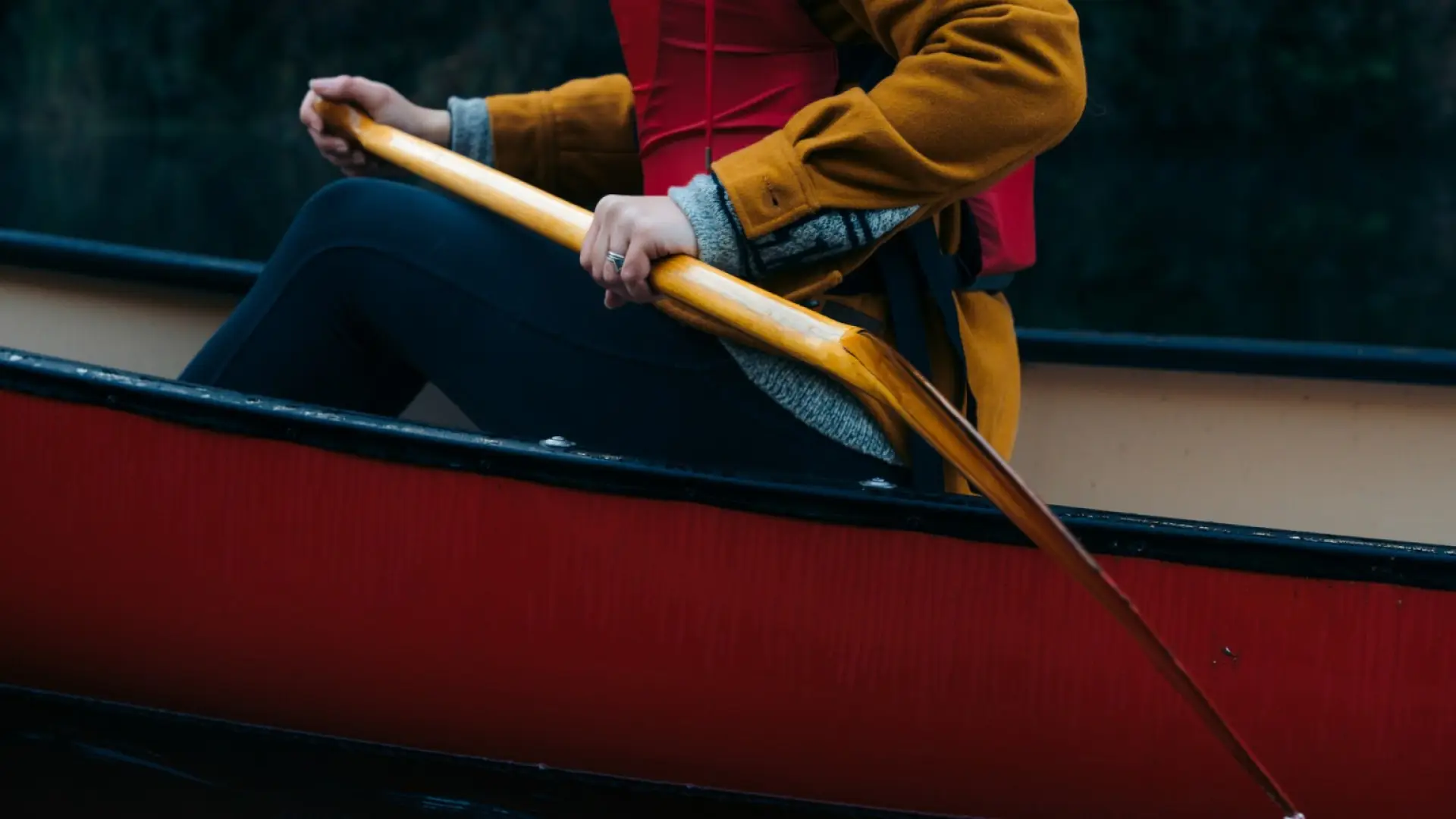 Shoulder down shot of person sitting in red canoe wearing red pfd holding wooden paddle