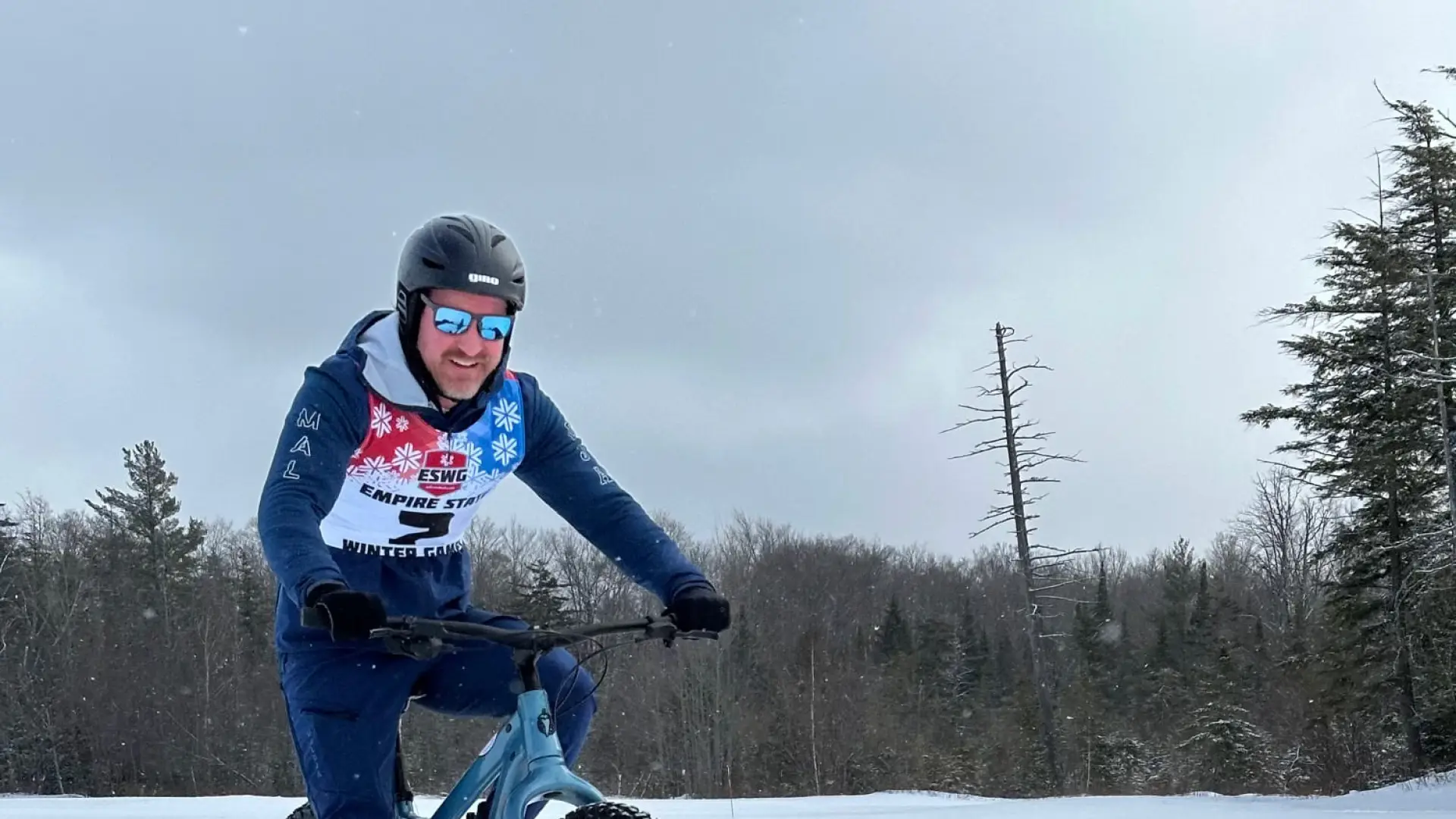 Cyclist in a helmet rides a fat-tire bike on a snowy trail, surrounded by a winter forest.