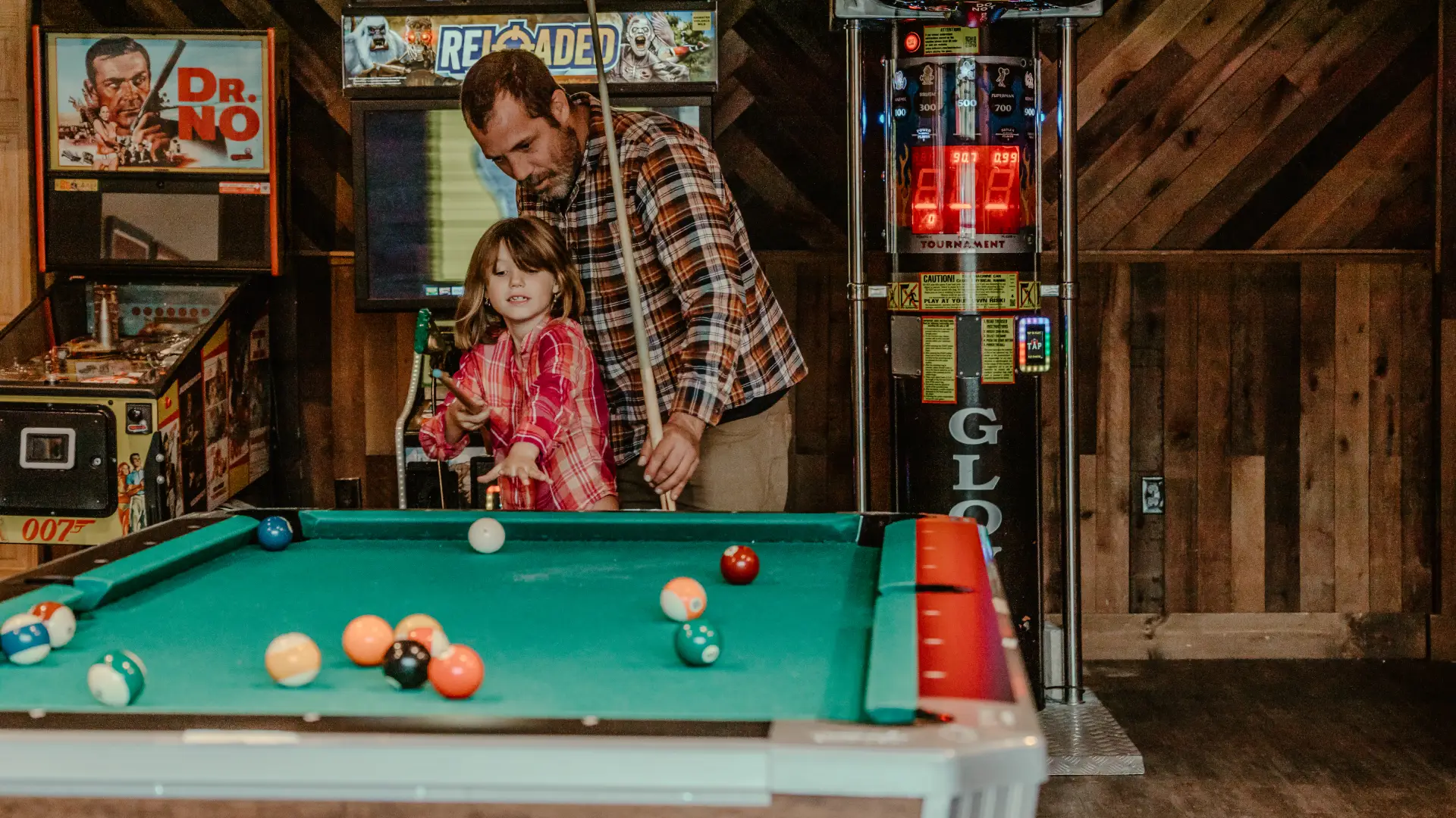A father and daughter play billiards with an assortment of arcade style games behind.  Photo Credit to A. Kelly.