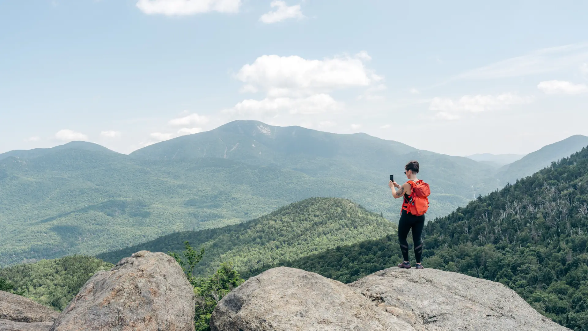 A woman takes a picture on top of a mountain. 