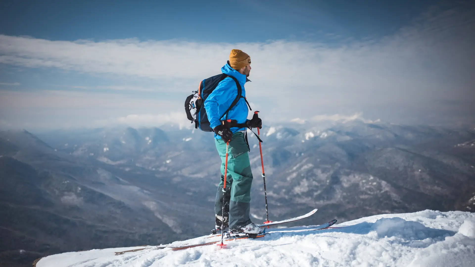 A man stands at the top of a mountain summit in winter.