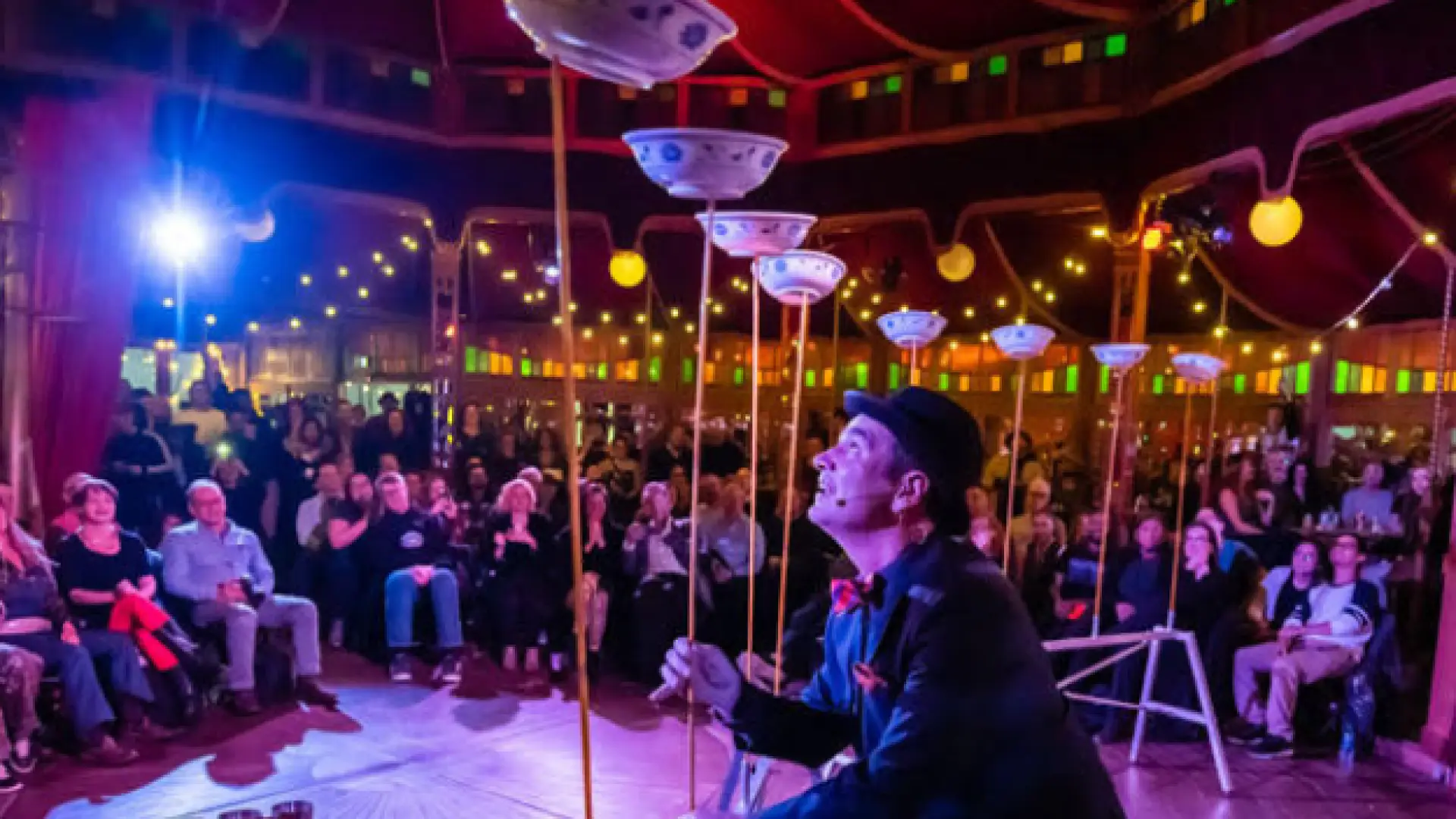 Circus performer spins plates on the wooden poles on stage in front of audience