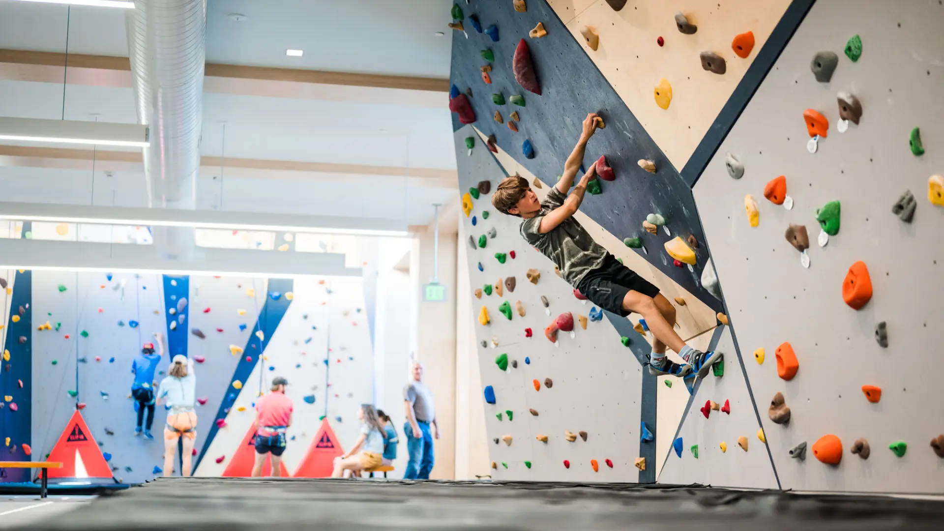 A teenage boy climbs a cantilvered indoor rock climbing wall.