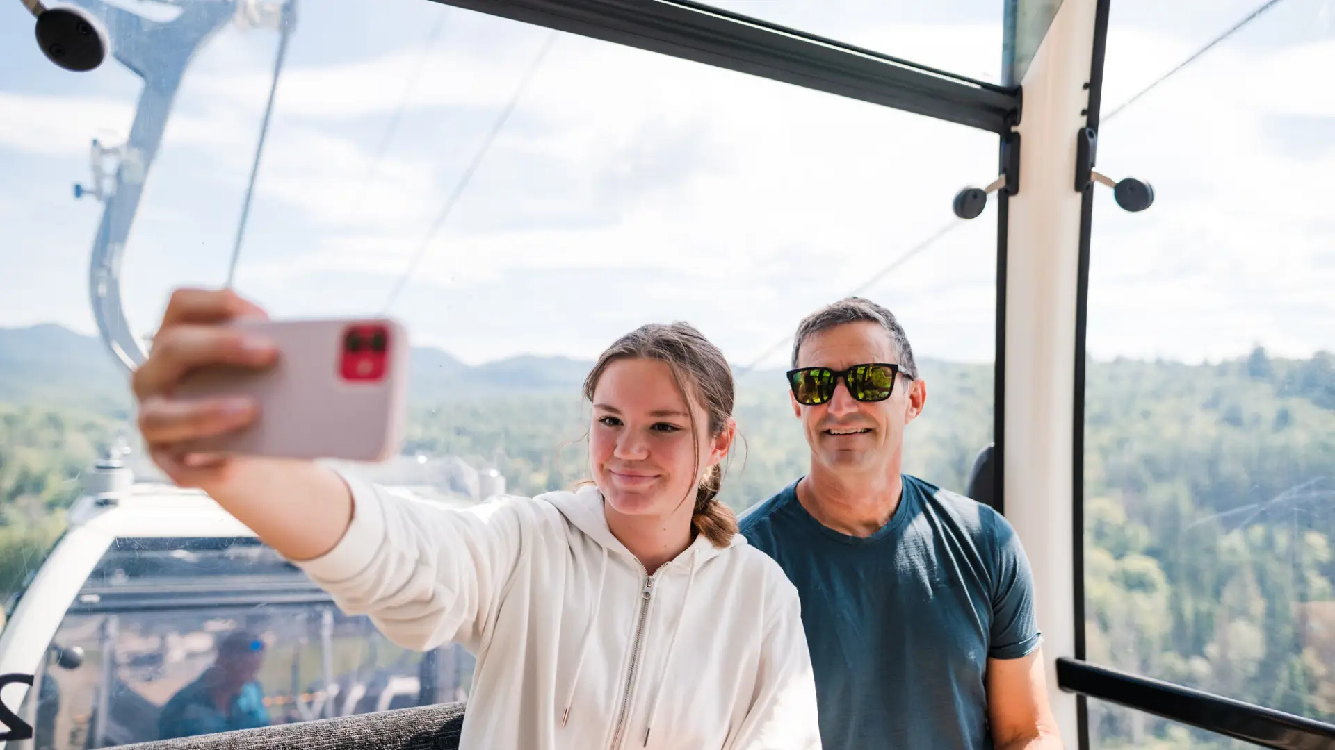 A teenage girl and an adult male smile for a selfie on a gondola.