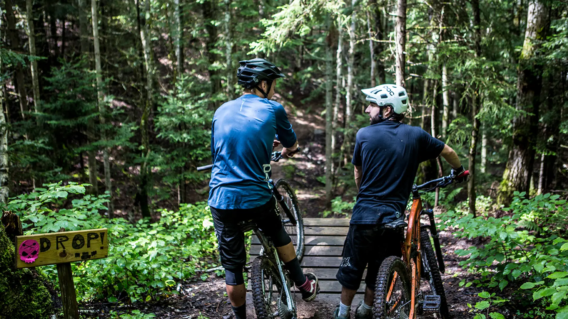 A pair of mountain bikers take a break before crossing a mountain biking bridge.