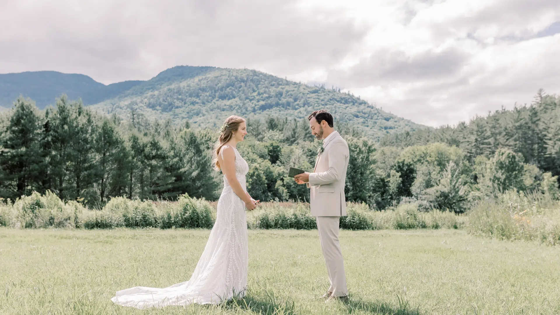 Bride and groom face each other in a grassy field with mountain views