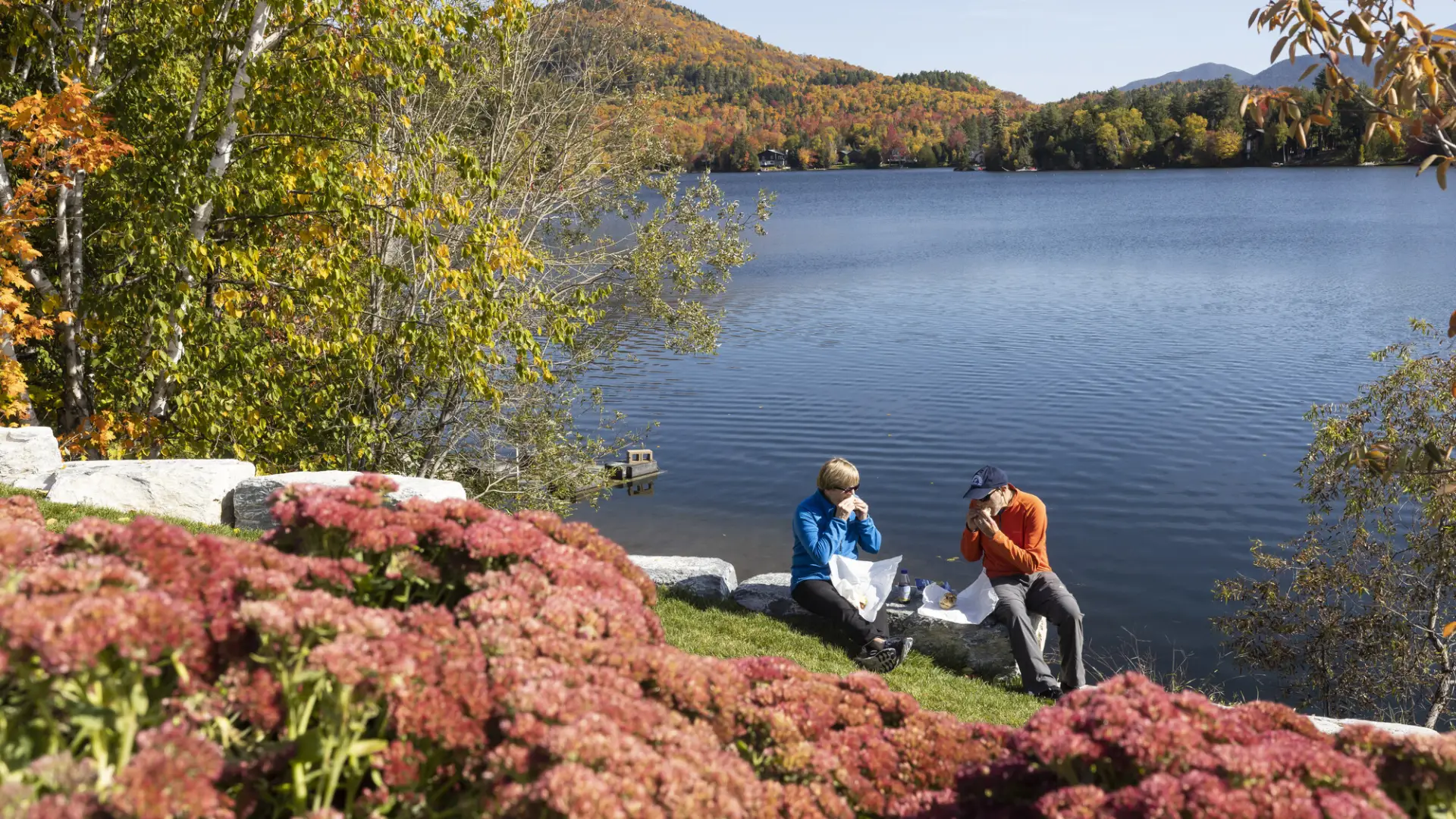 Two people eat lunch on the edge of a lake