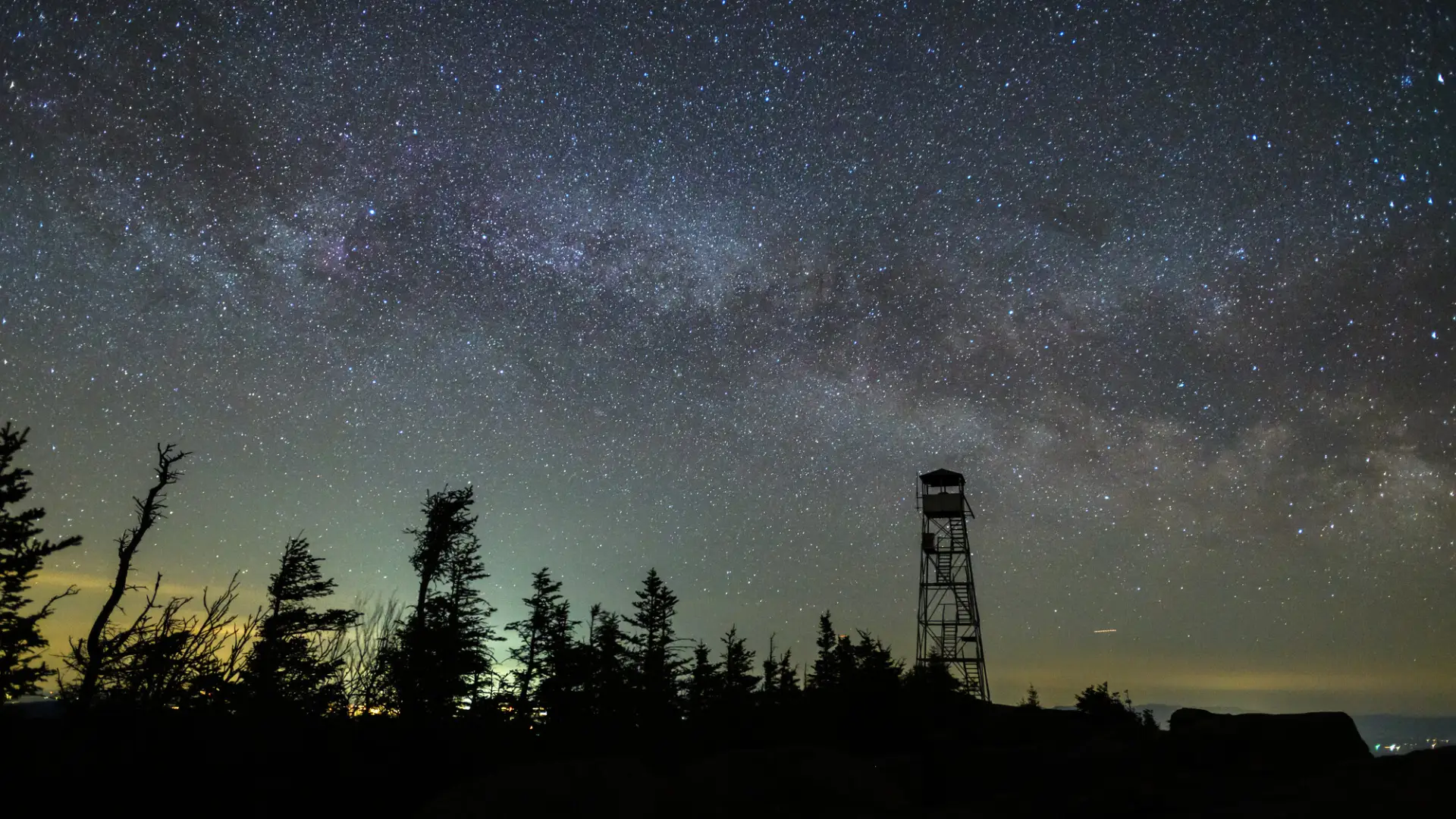A starry night sky behind a fire tower.