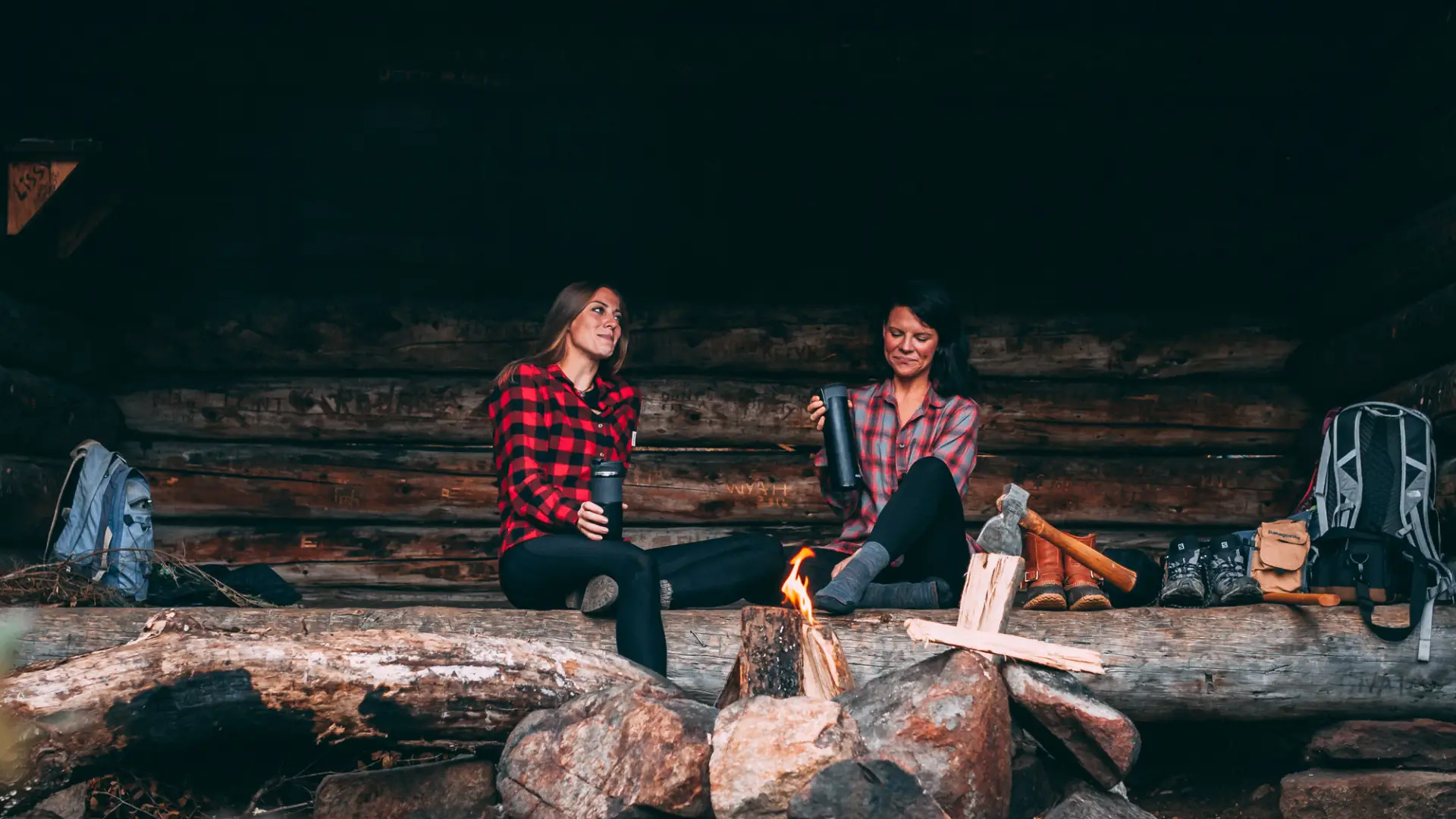 Two women in flannels talk in a lean-to.