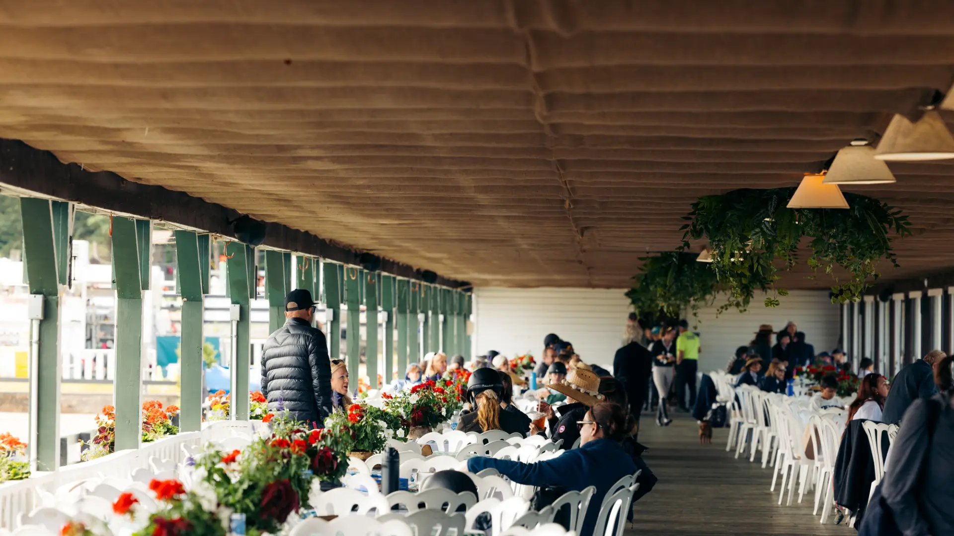 A few people sit at rows of white round tables and chairs in pavilion building