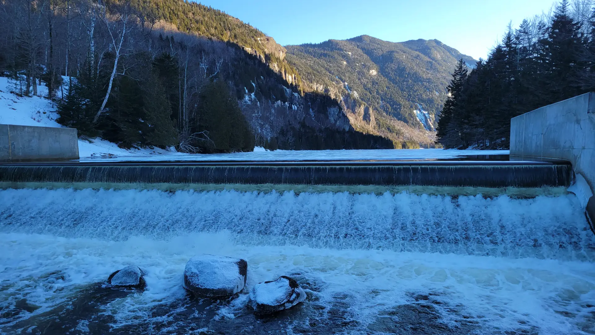 A long dam with water spilling over the top in the winter