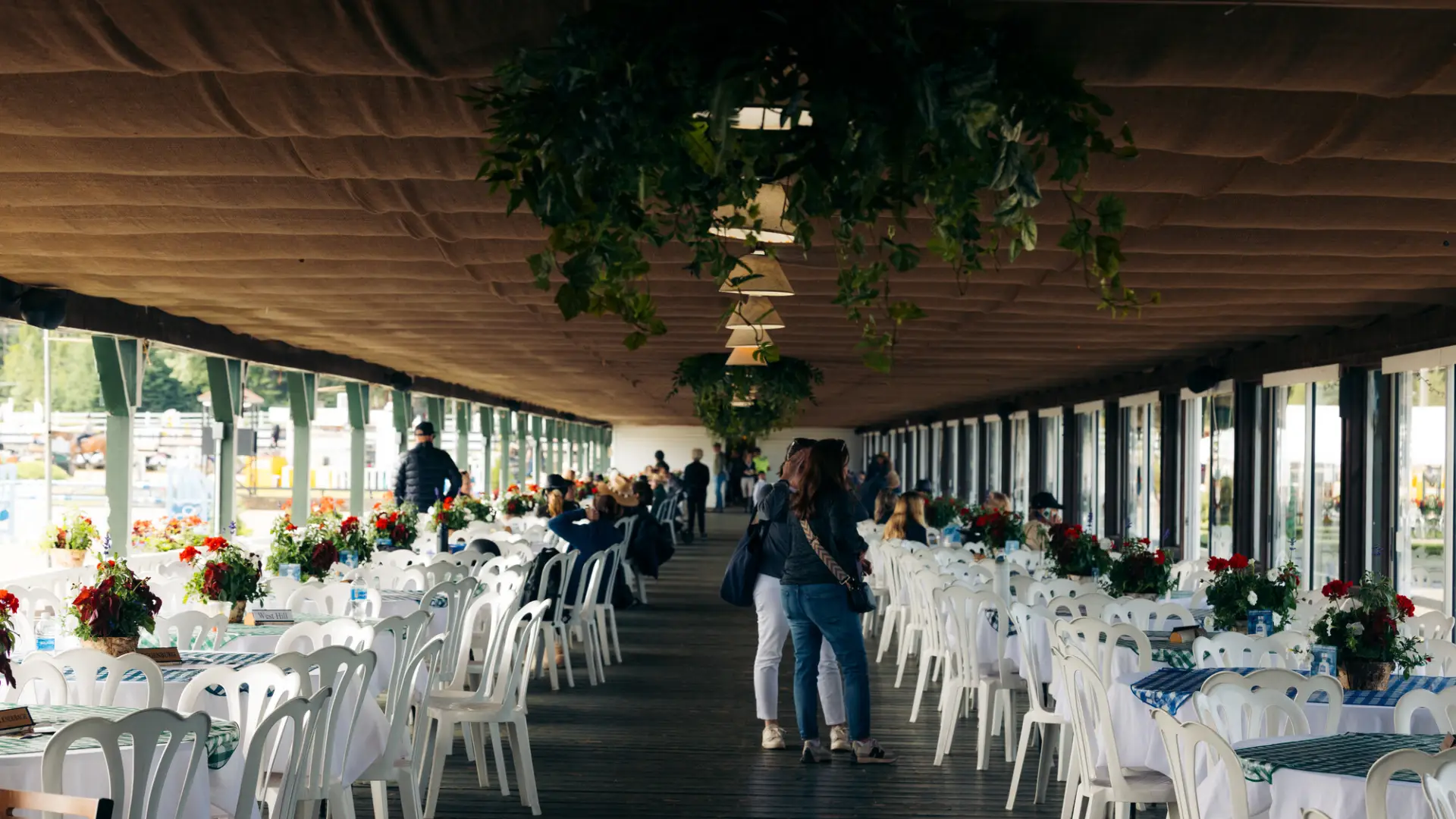 Two rows of round white tables and chairs line either side of pavilion building with some people standing in aisle