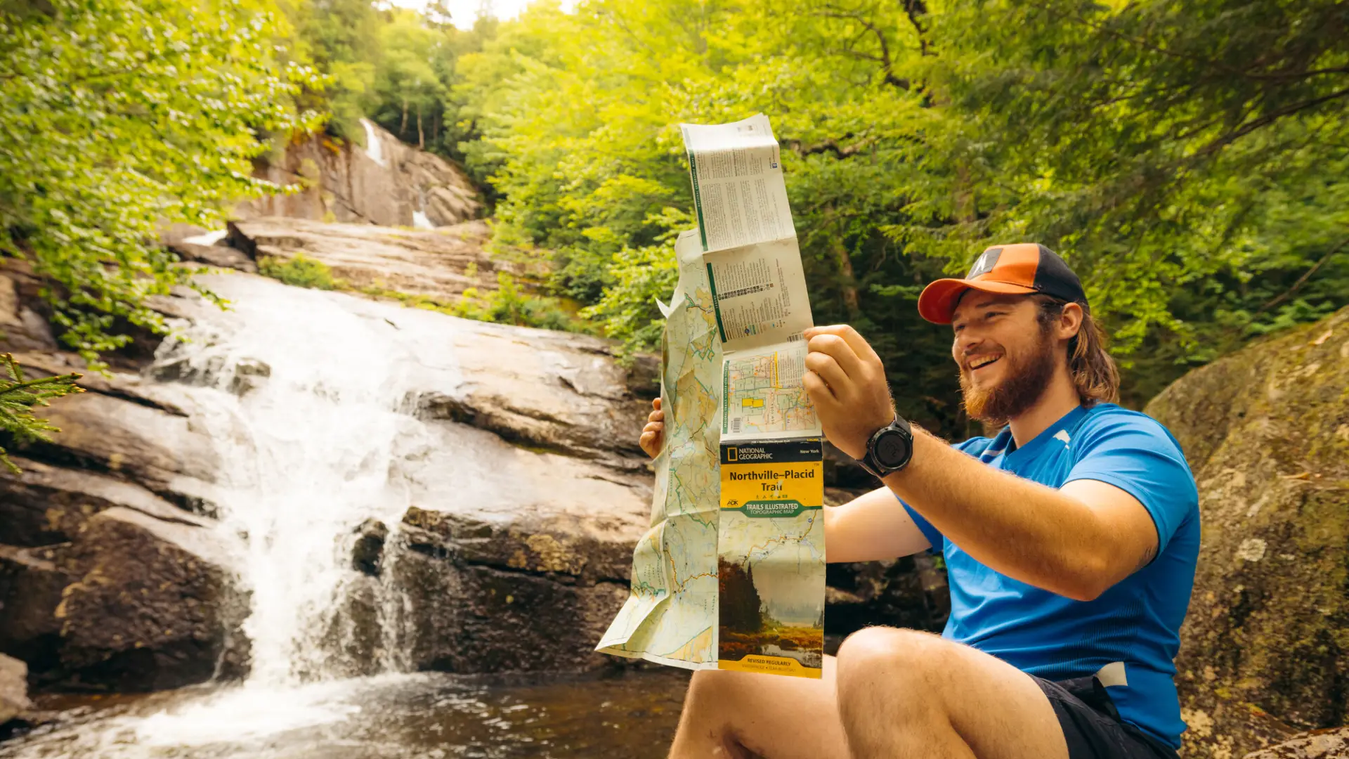 A hiker checks his map in front of a waterfall