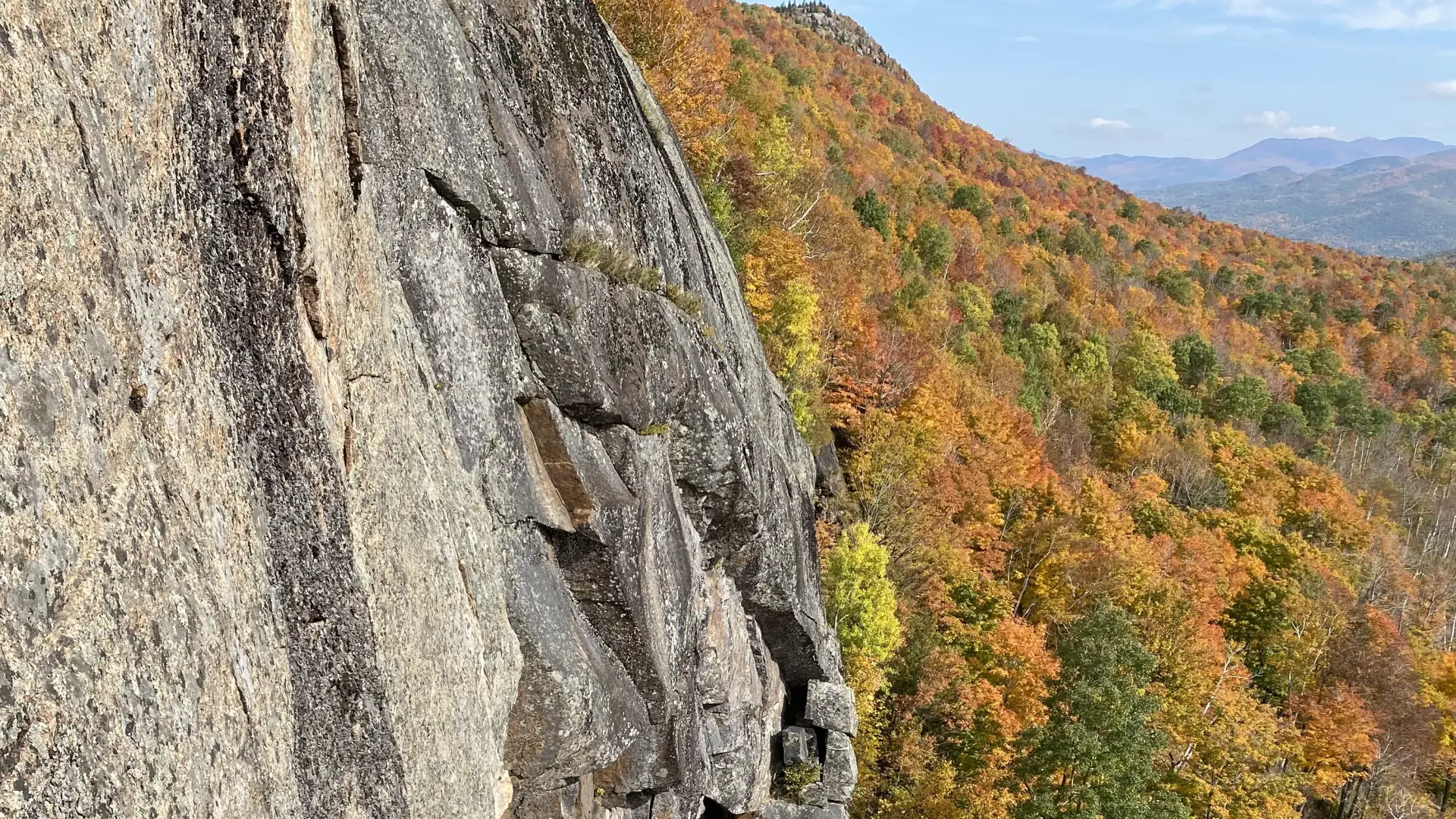 A steep rock wall with bright orange trees below