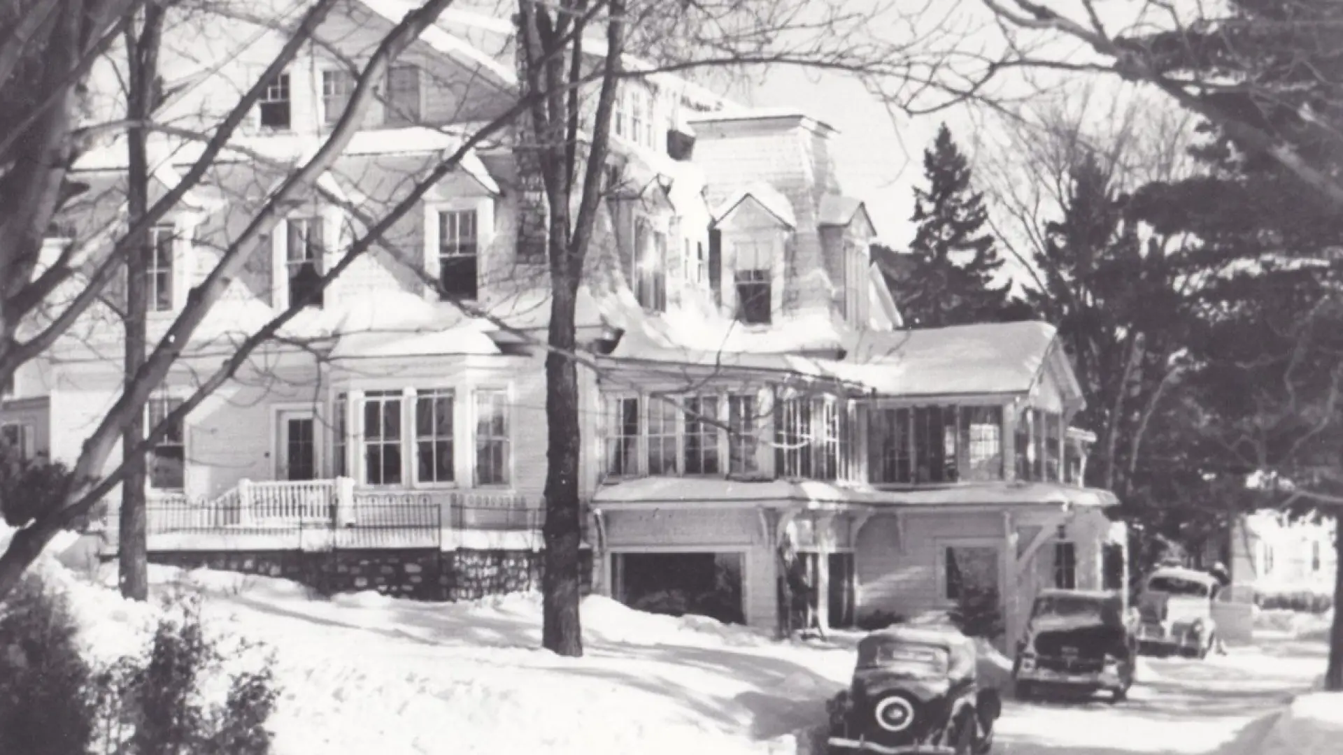 Vintage black and white photograph of the original Mirror Lake Inn, with early automobiles parked on the drive. Image courtesy Mirror Lake Inn.