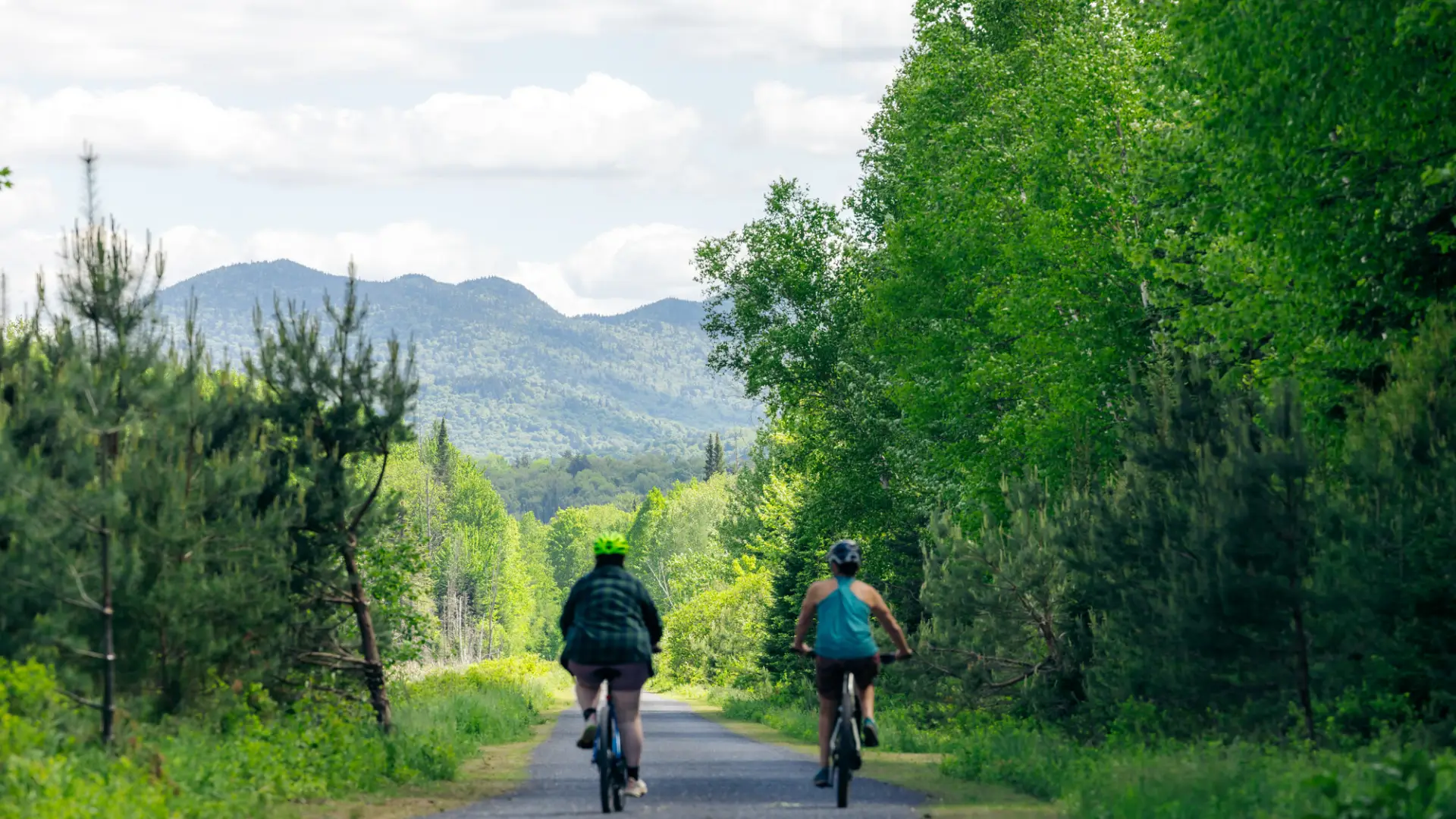 Two women ride bicycles on a backcountry path. 