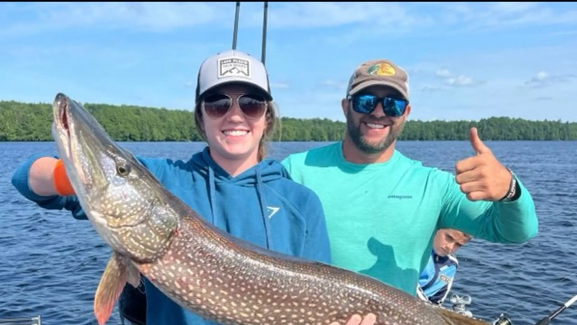 Two people holding a giant pike while giving thumbs up.