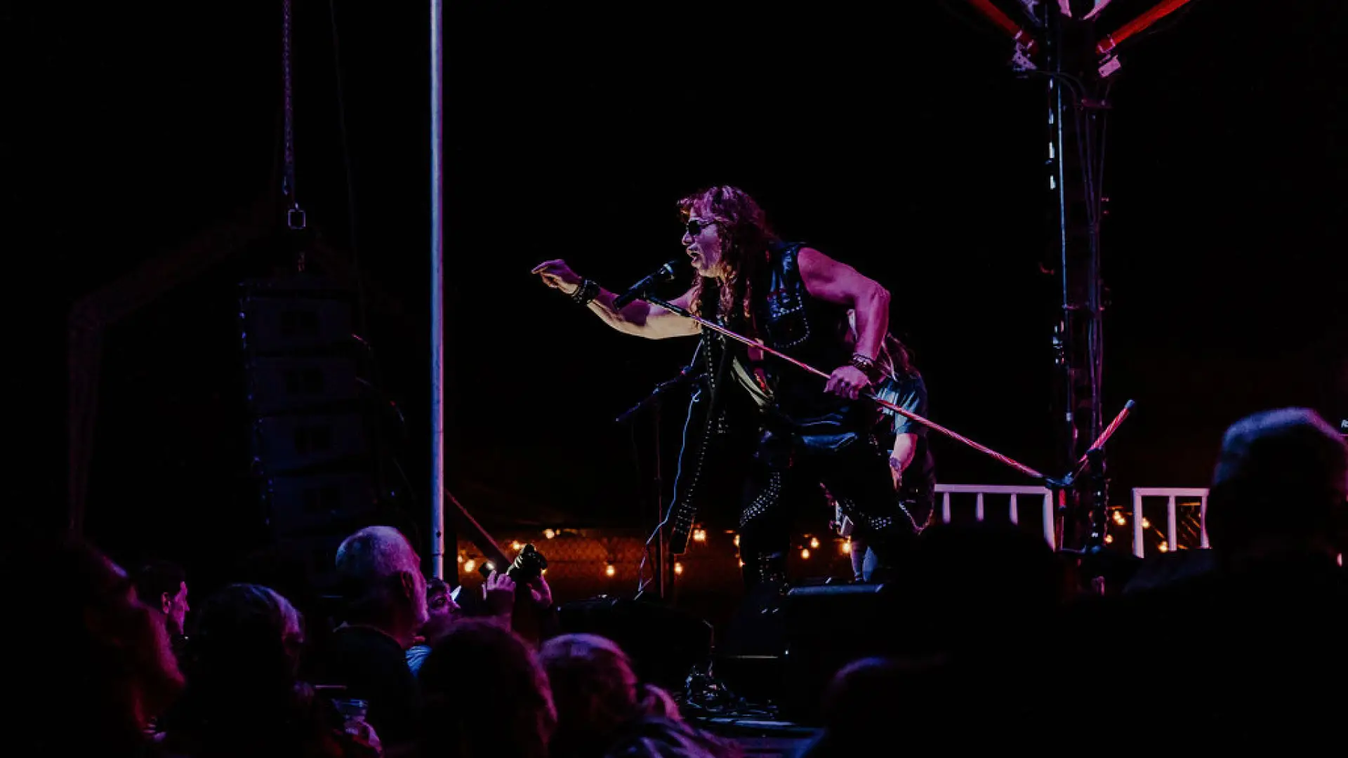 Singer leans out over stage singing in dark outdoor setting with crowd in front of the stage