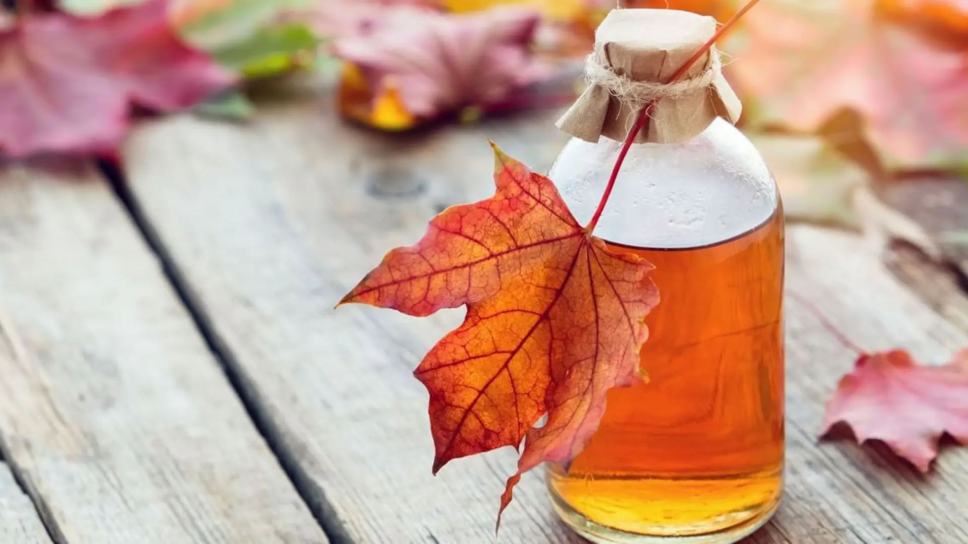 A small jar of maple syrup surrounded with fallen leaves and tied with jute twine