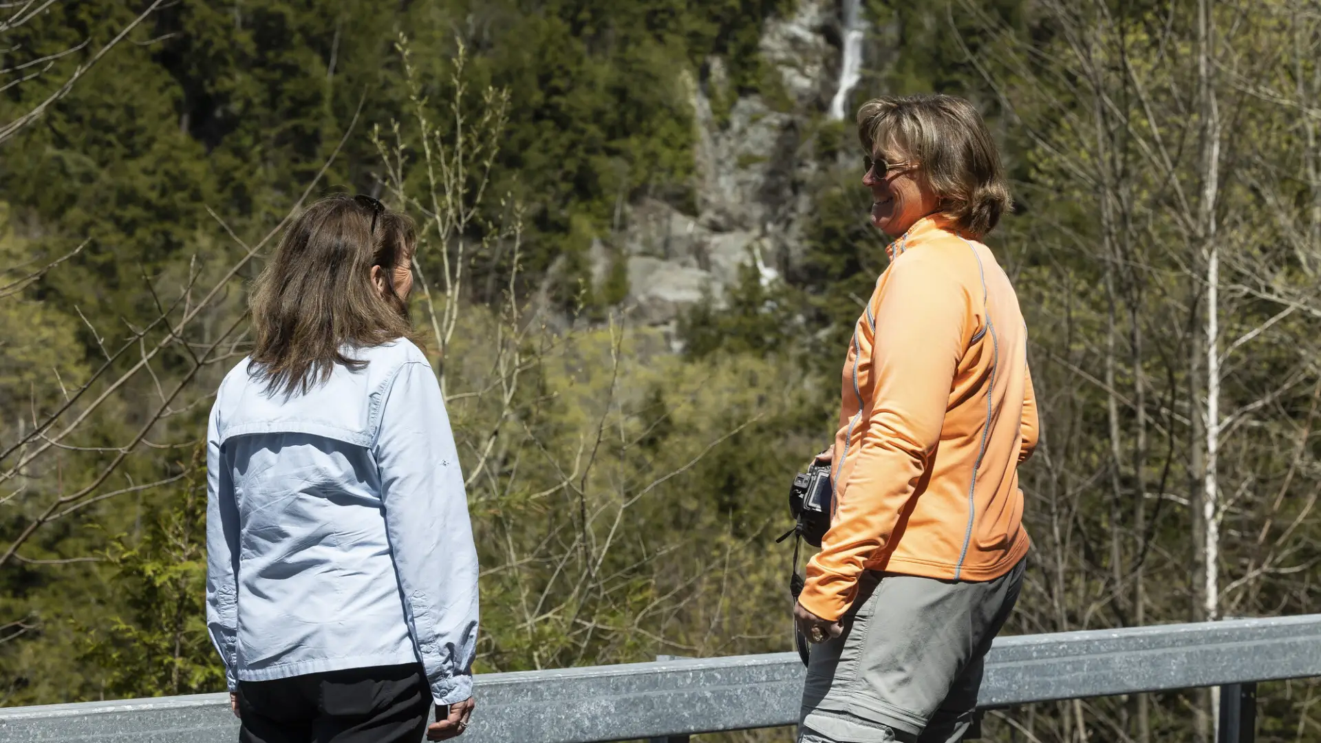 Two woman standing on the side of the road in front of a waterfall