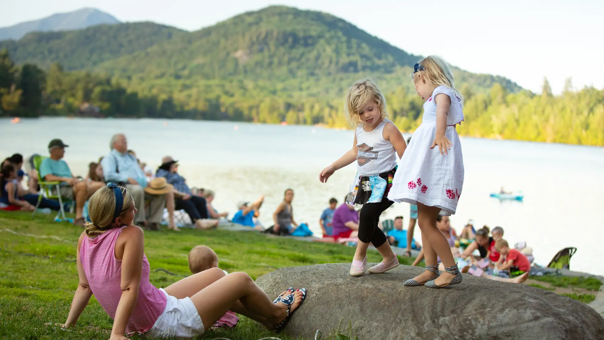 Kids dance on a rock in Mid's Park with Mirror Lake and the mountains in the backdrop
