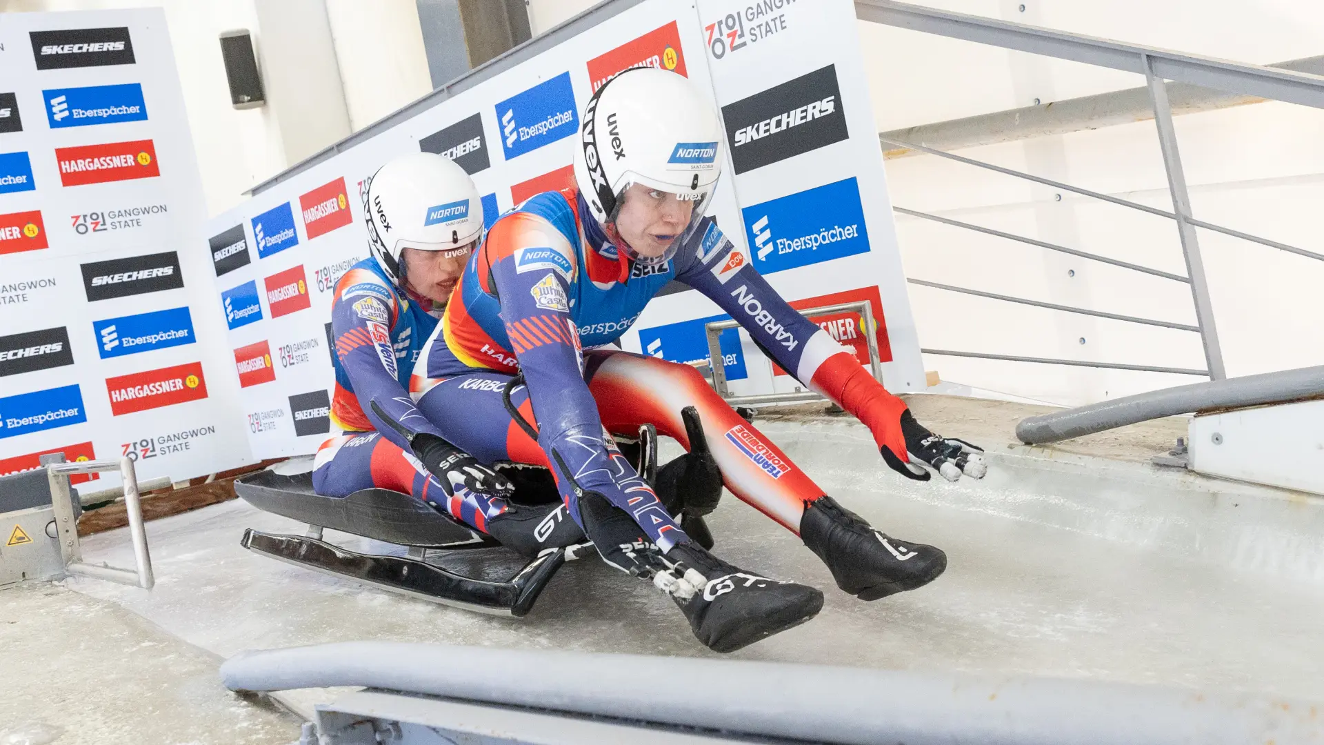 Two women's doubles luge athletes racing down an icy track.