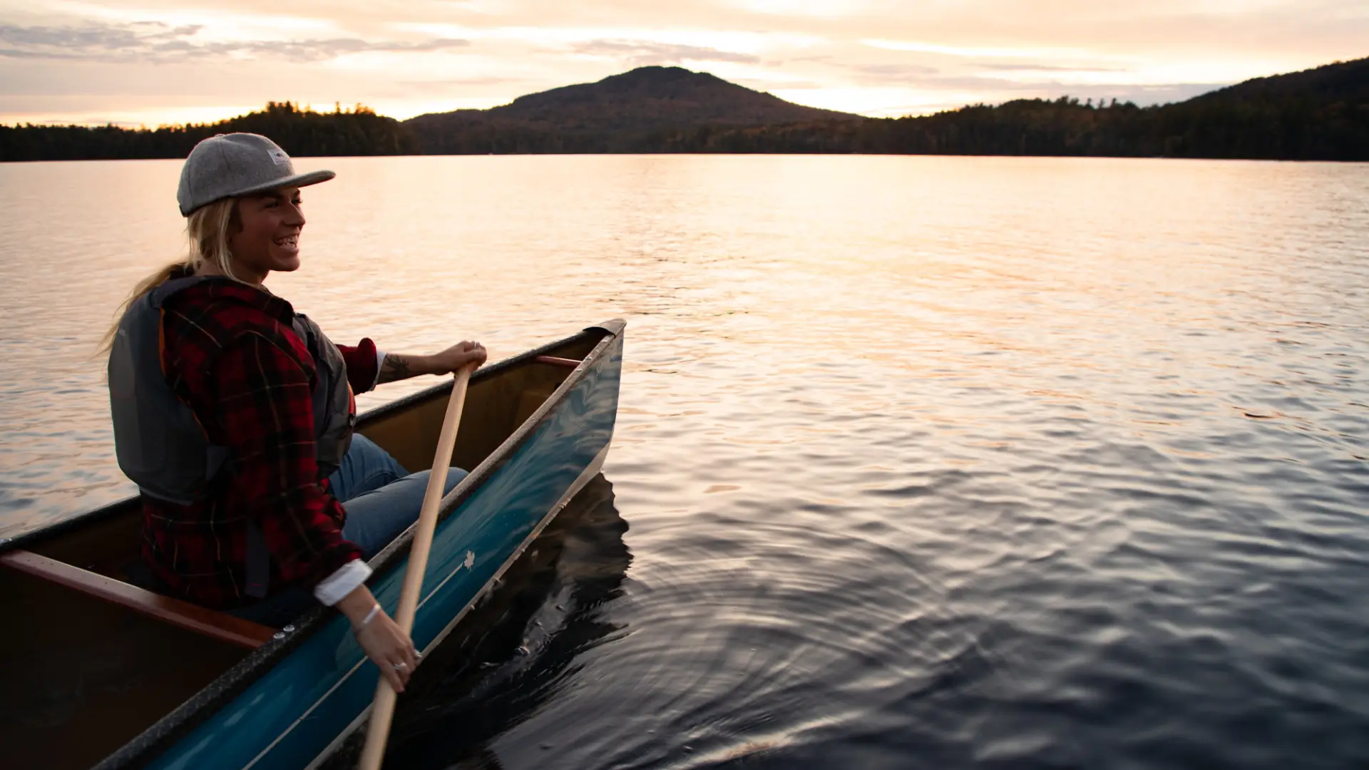 A woman paddling a canoe on a lake during sunset.