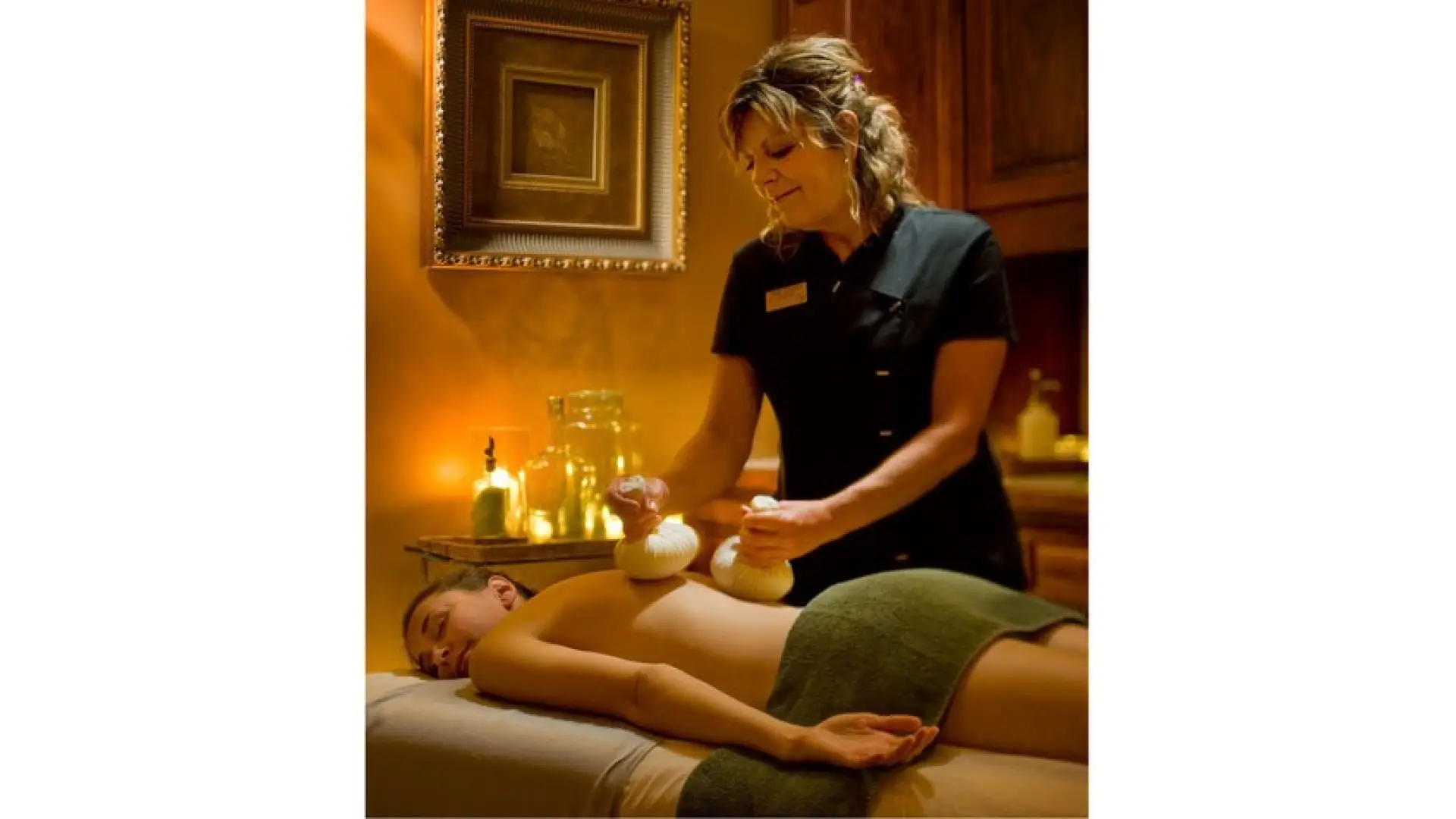 A massuse administers a thai herbal massage to a relaxed woman in a comfortable private room