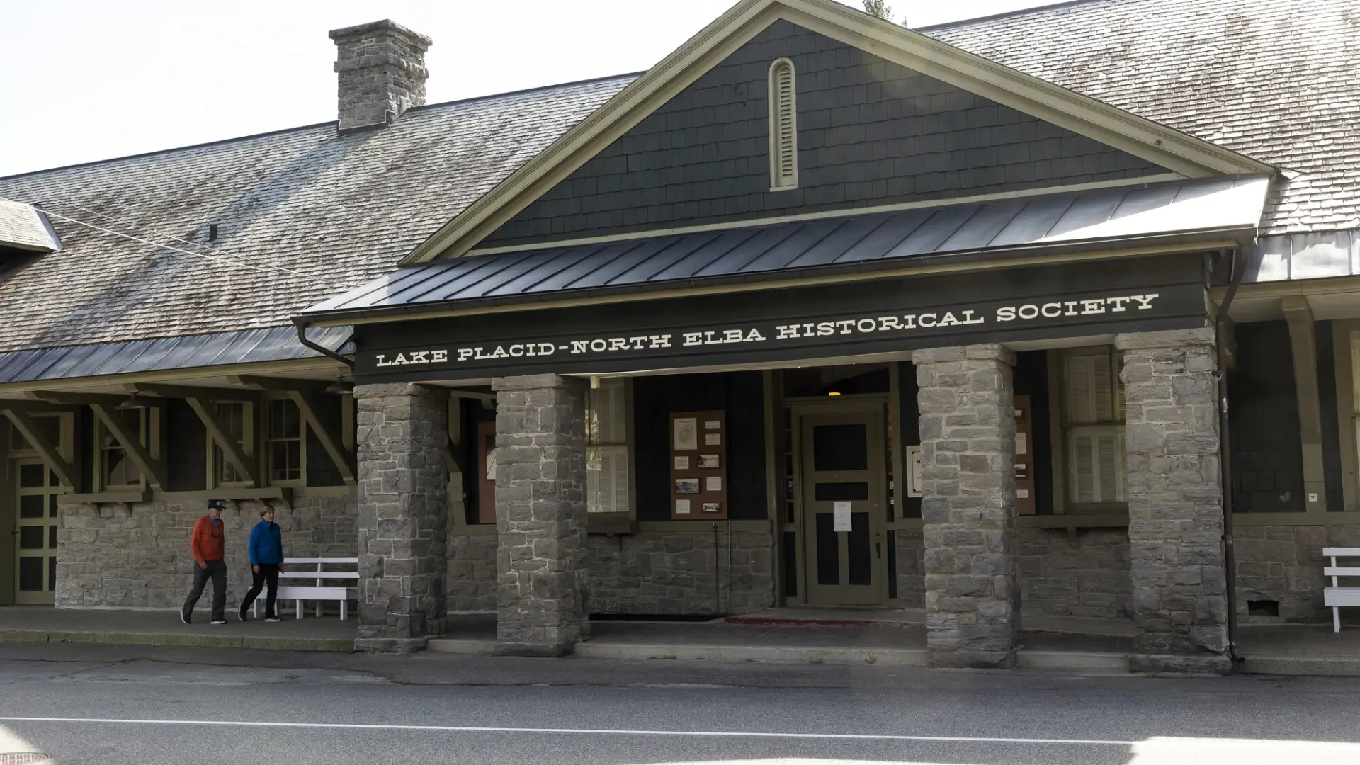 Two people walk on covered walkway up to the doors of the Lake Placid–North Elba Historical Society & Museum