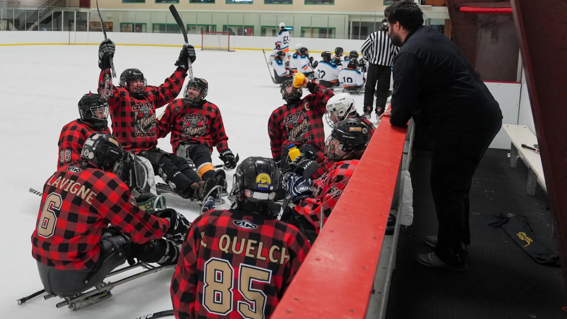 A sled hockey team in plaid jerseys celebrates on the ice during a game, showcasing camaraderie and excitement.