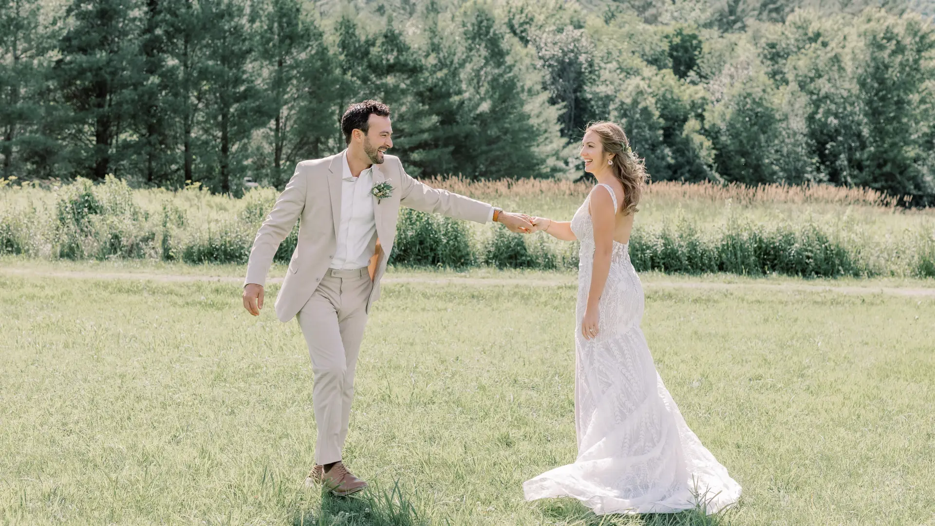 Bride and groom laugh and dance in a grassy field