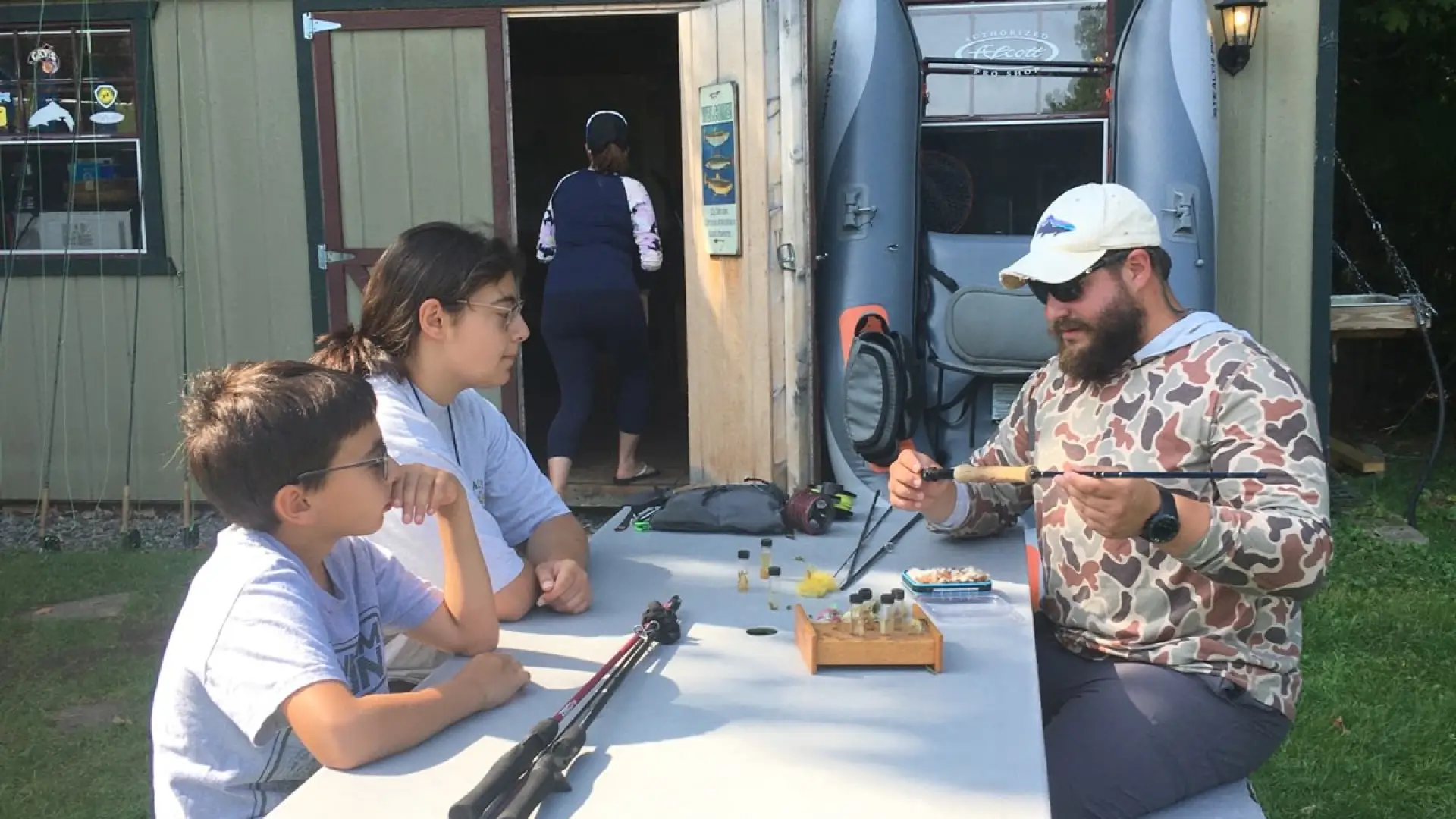 A family sits at a picnic table outside a guide house, preparing fishing gear.