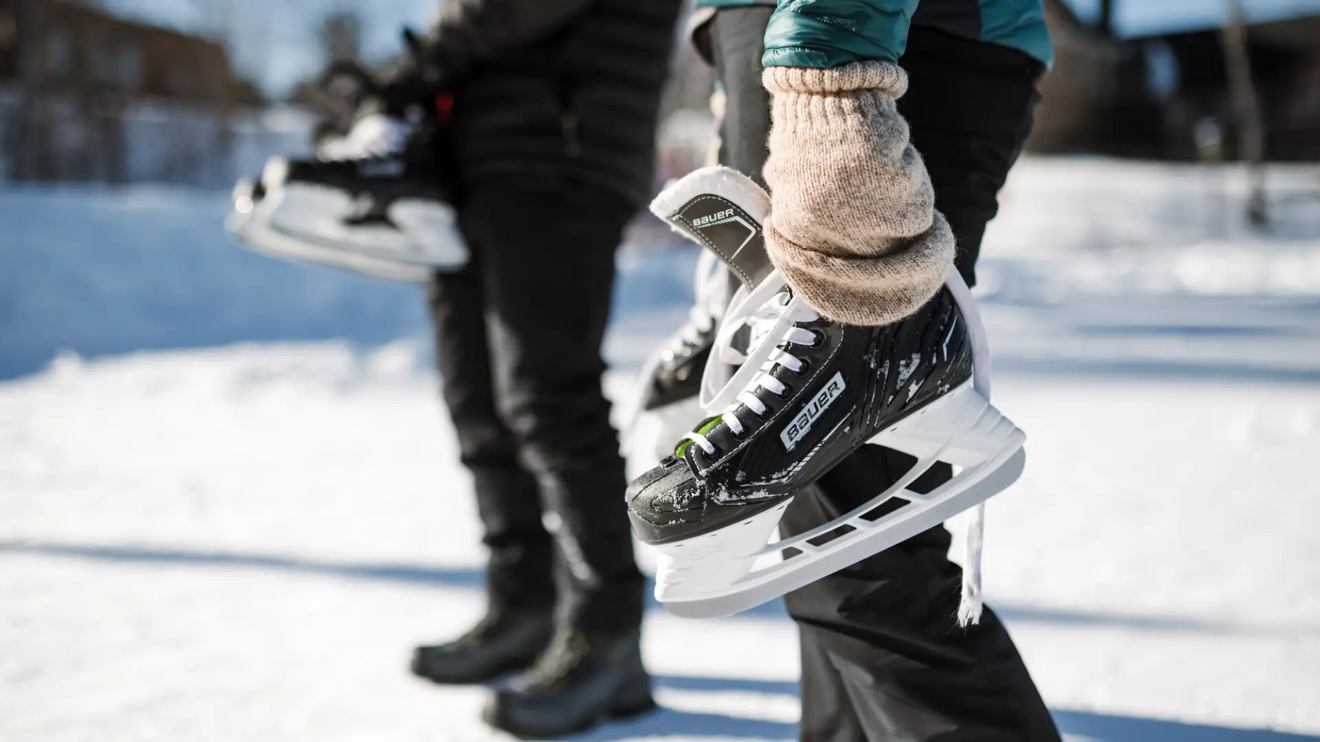 Two people each carrying a pair of black Bauer ice skates with white blades.