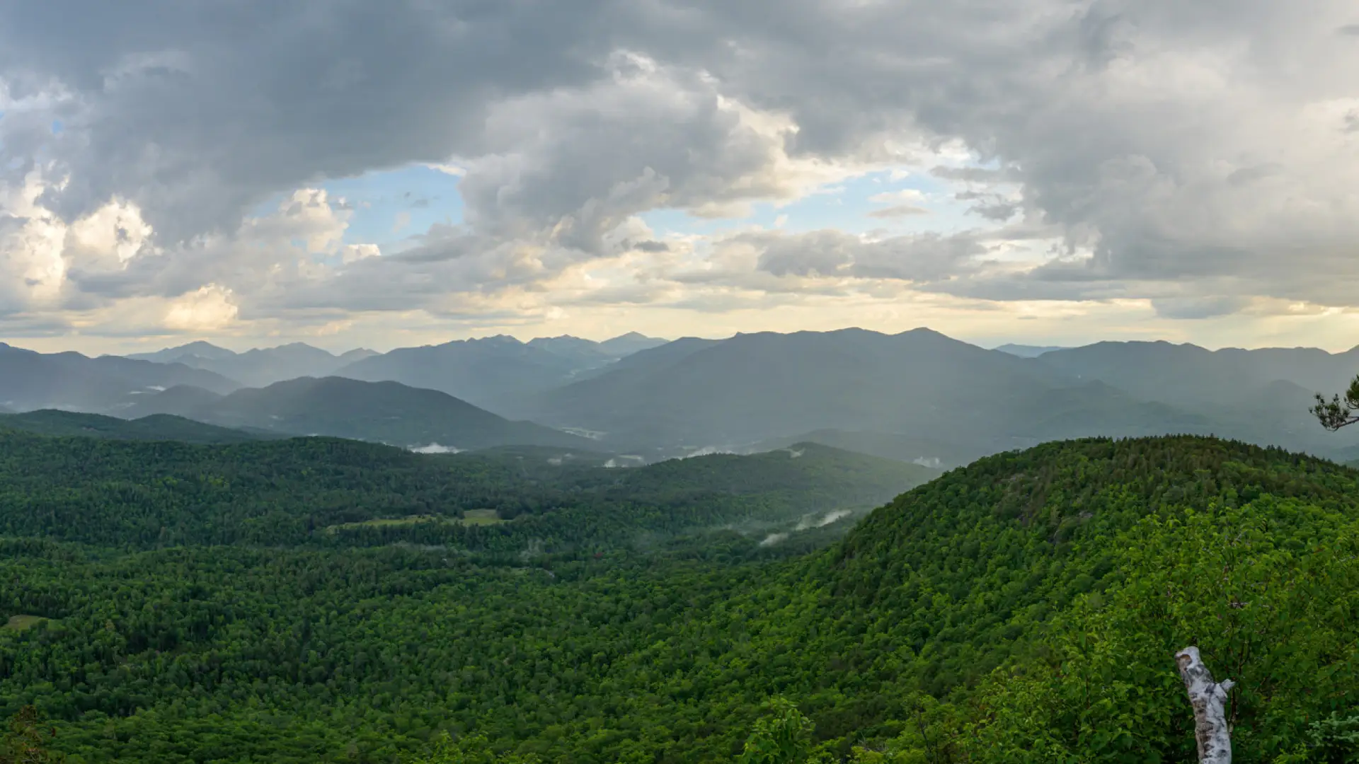 A view from the summit of a mountain with clouds and summer mountain views.