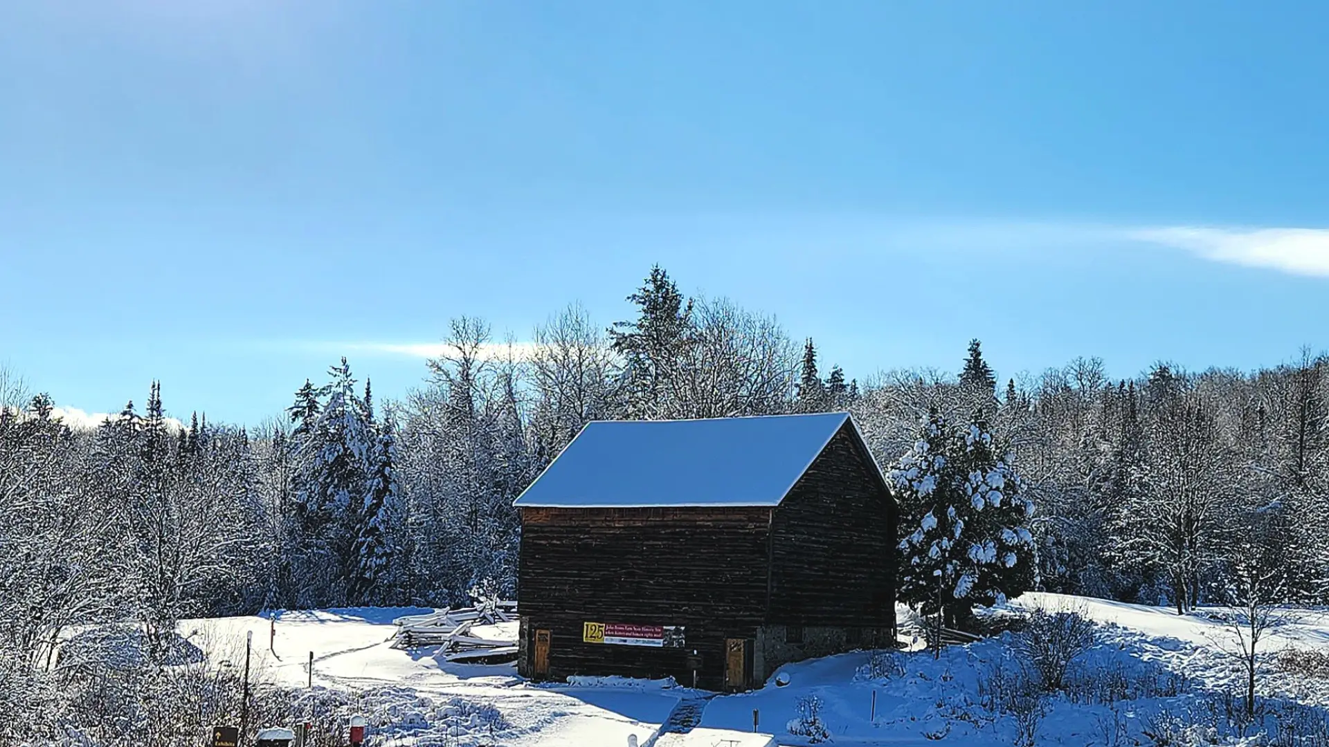 Small brown barn on John Brown Farm with snowy roof and snow on ground on blue sky winter day