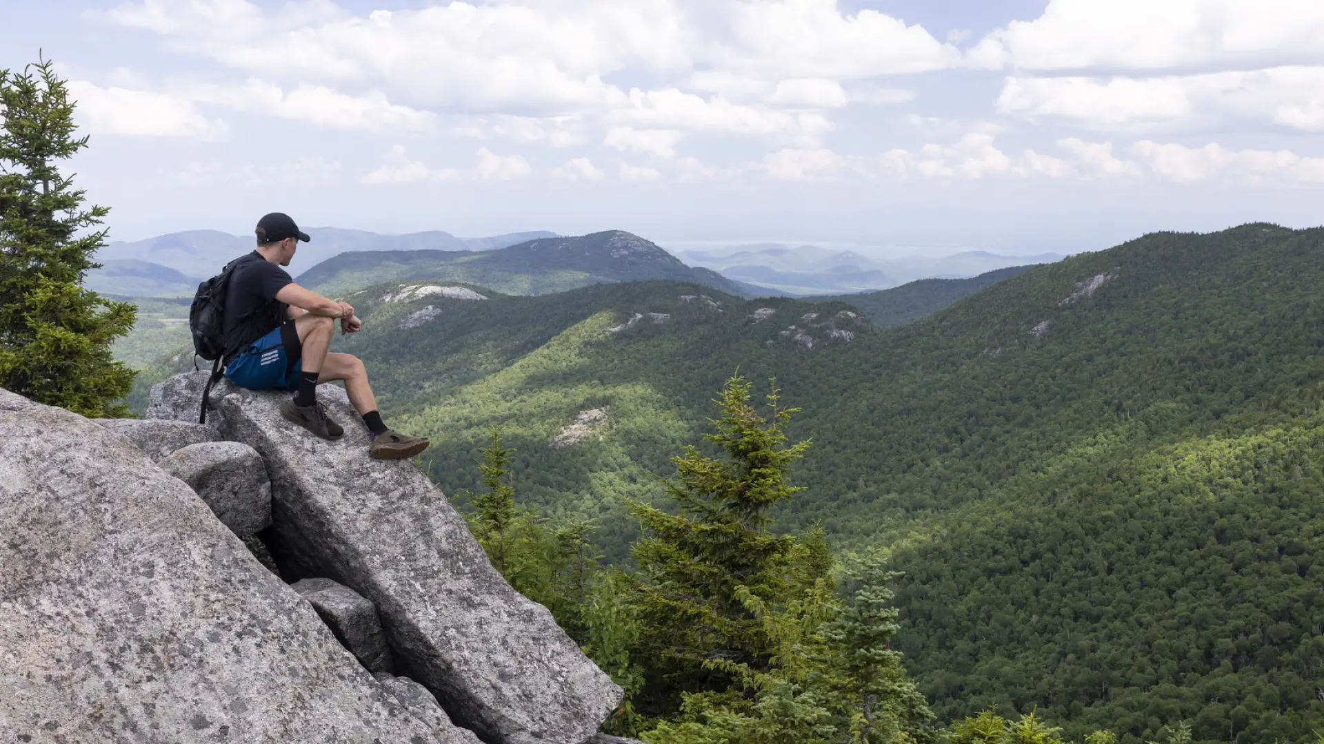 A hiker sits on a large rock on a summit