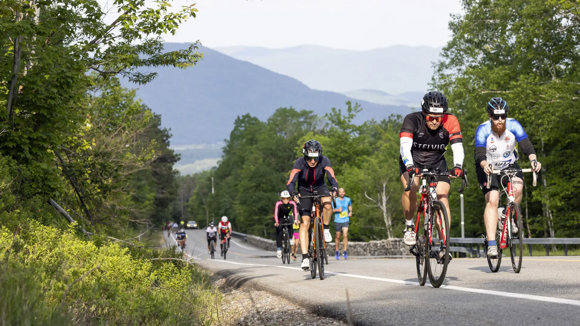 A group of cyclists going up a road with mountains behind them